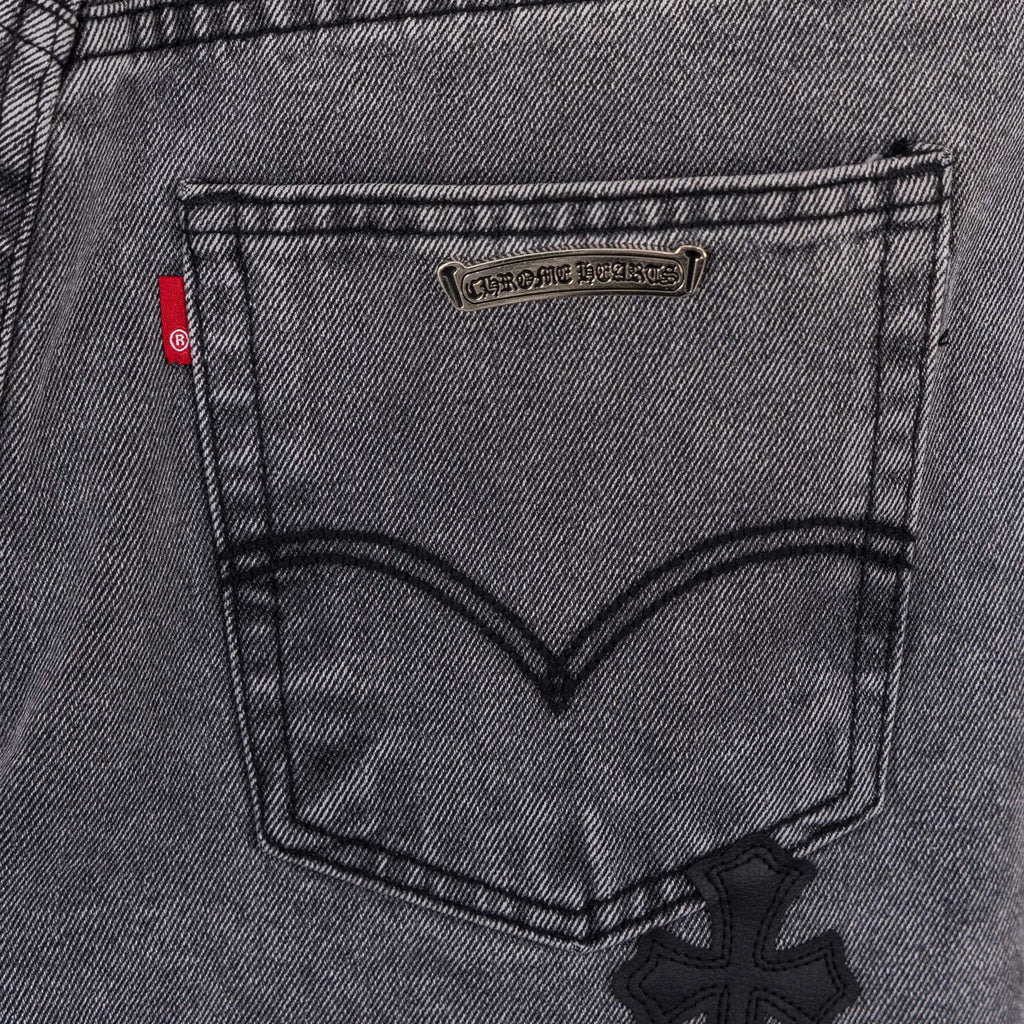 Gray denim pants back pocket close-up with small brand patch and cross applique