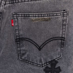 Gray denim pants back pocket close-up with small brand patch and cross applique