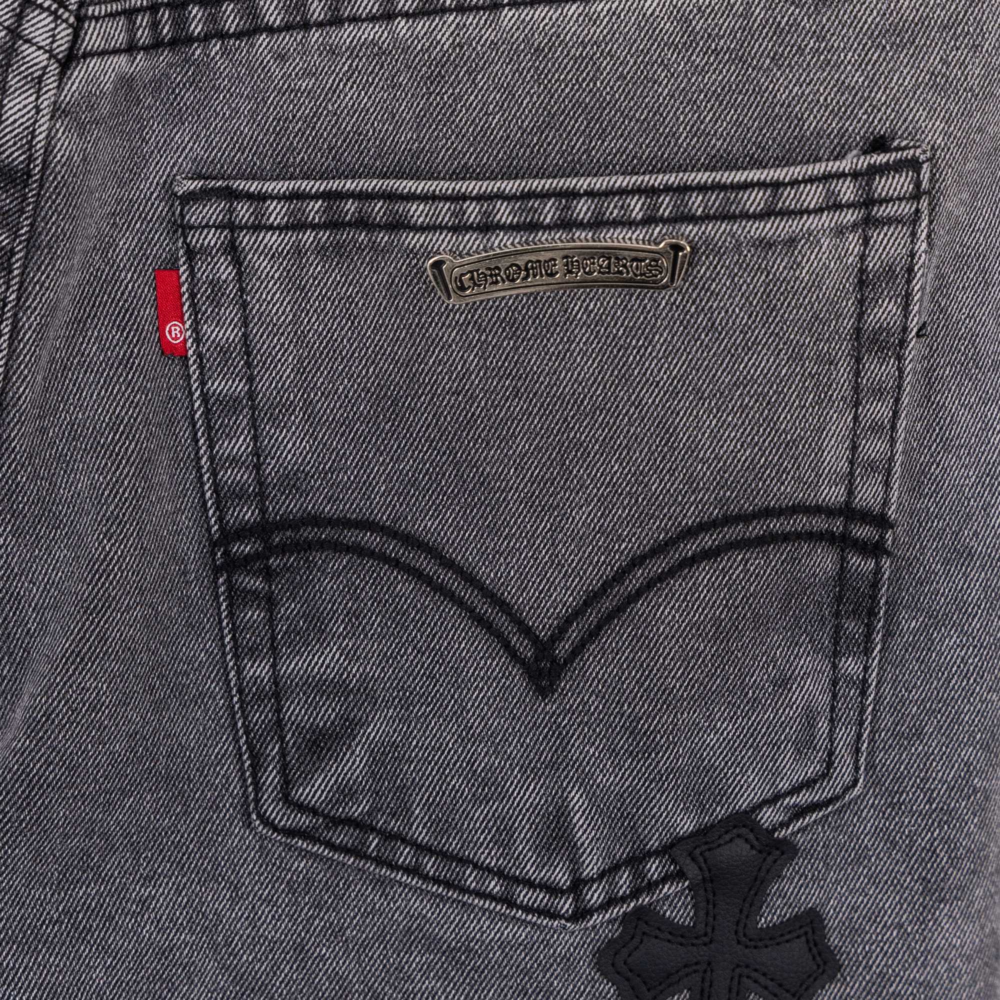 Gray denim pants back pocket close-up with small brand patch and cross applique