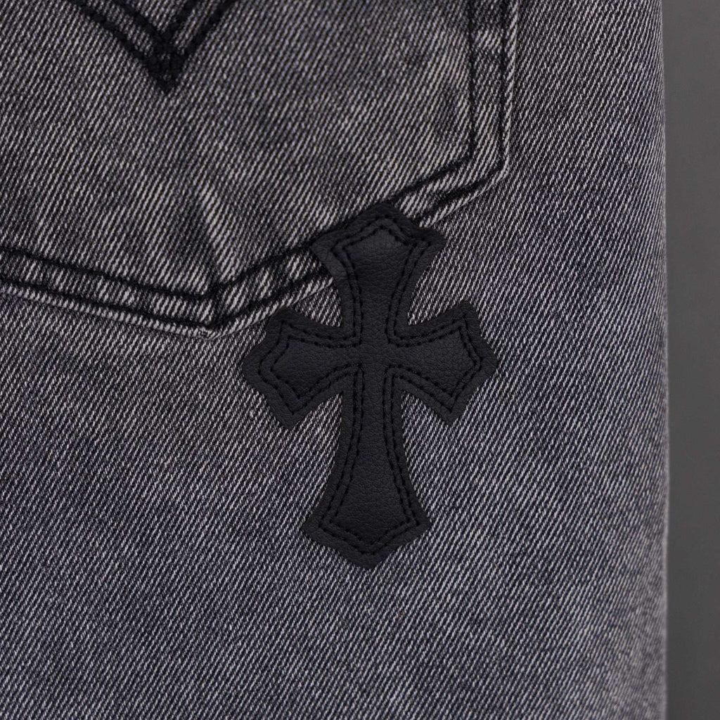 Gray denim pants close-up of small black cross applique on fabric