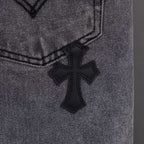 Gray denim pants close-up of small black cross applique on fabric