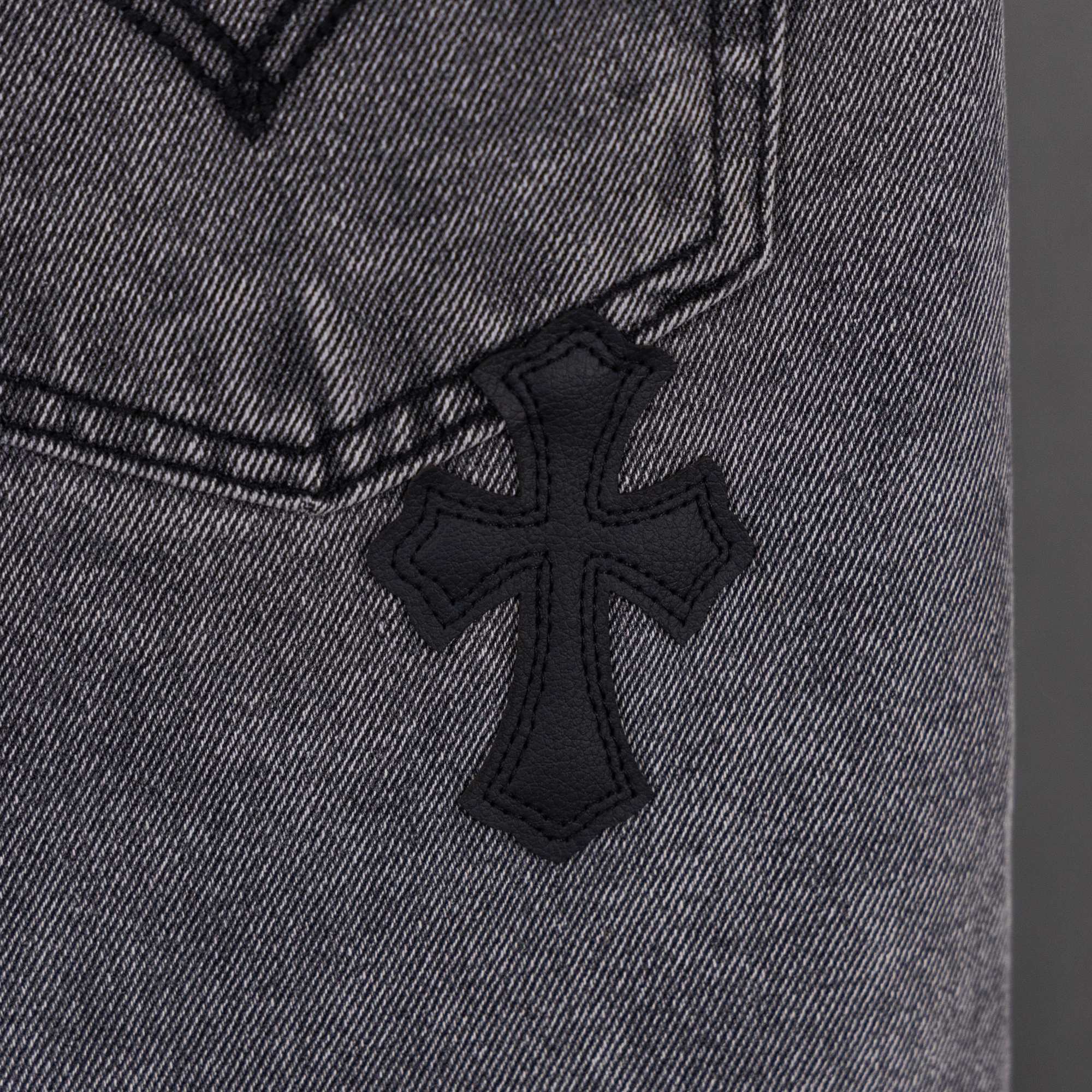 Gray denim pants close-up of small black cross applique on fabric