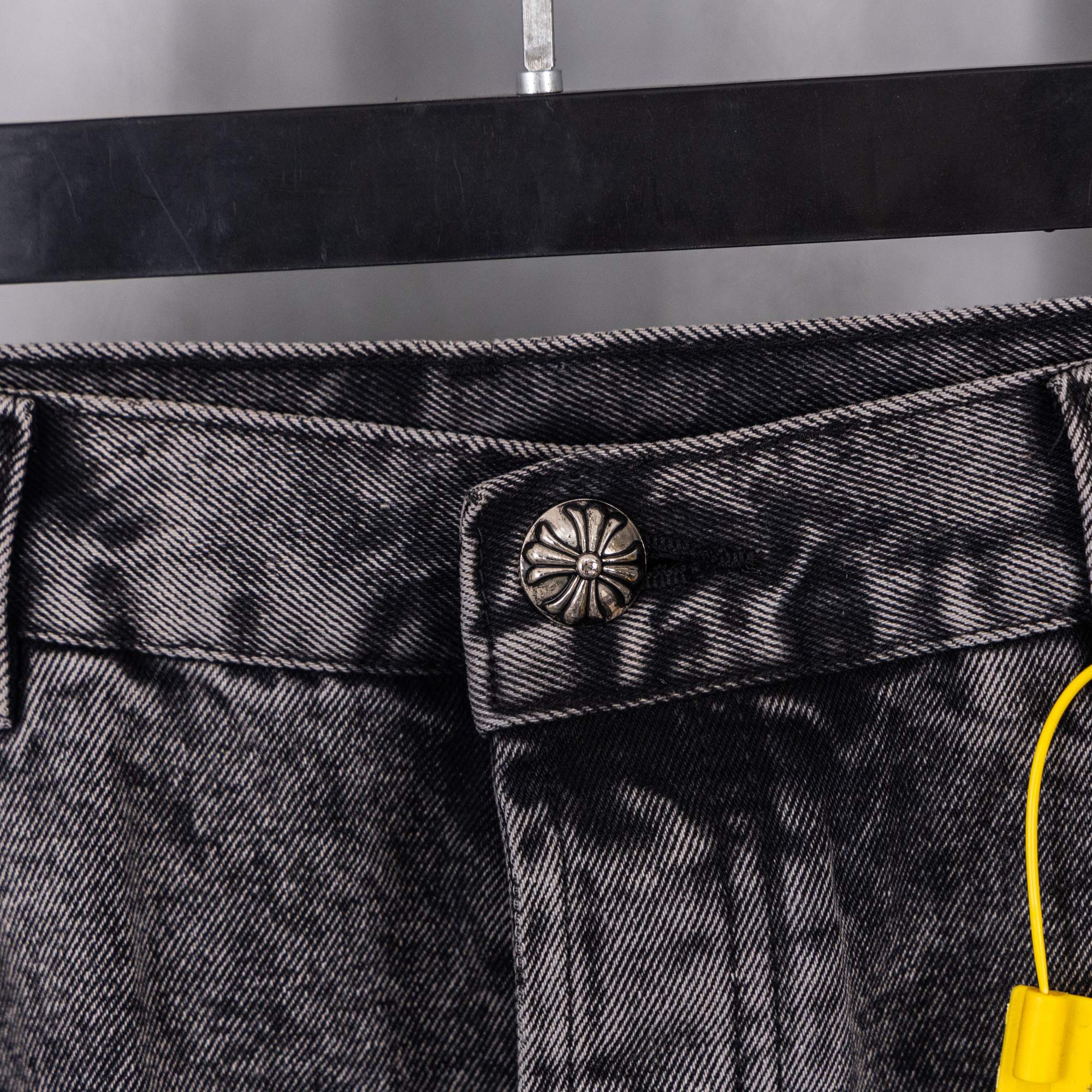 Denim pants waistband button area with metal tab and yellow tag string.