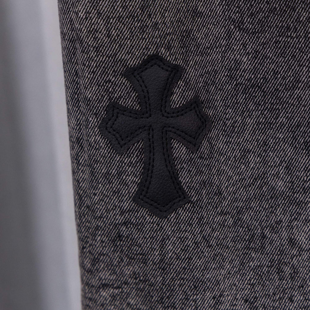Black cross appliqué on gray denim pants front.