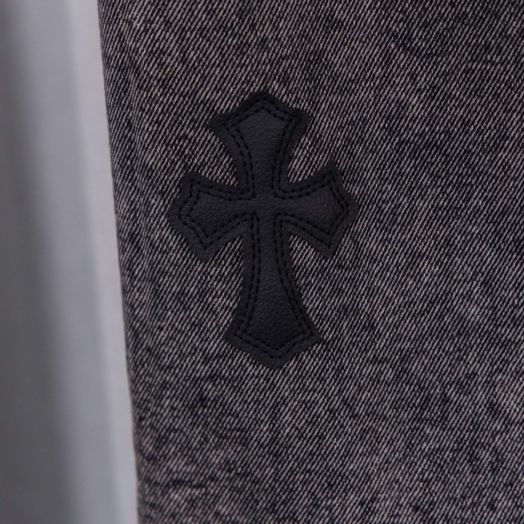 Black cross appliqué on gray denim pants front.