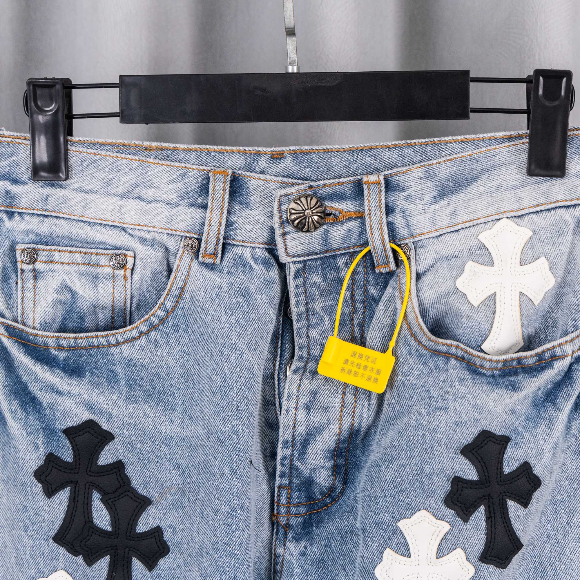 Light blue denim jeans close-up: front pockets with cross patches.