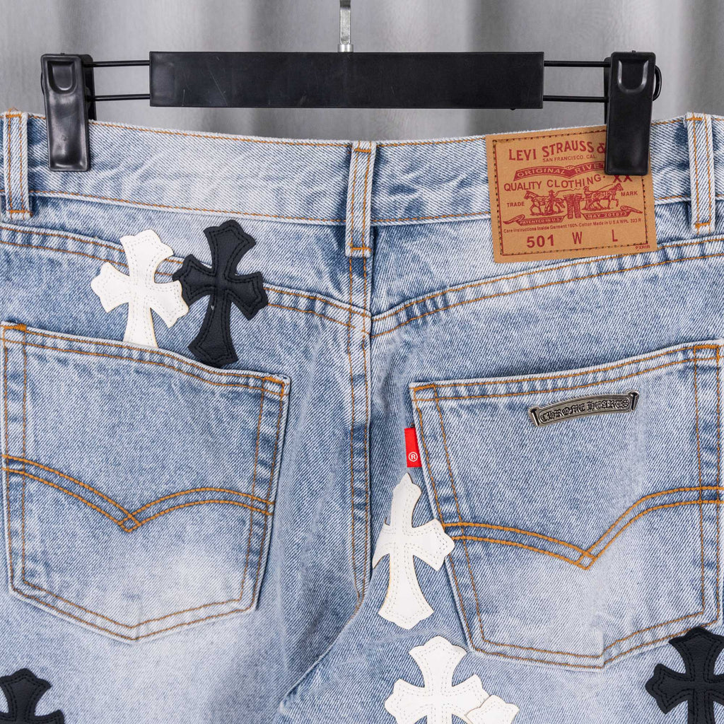 Light blue denim jeans close-up: back pockets with cross patches and label.