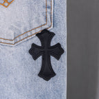 Black cross applique on light blue denim jeans.