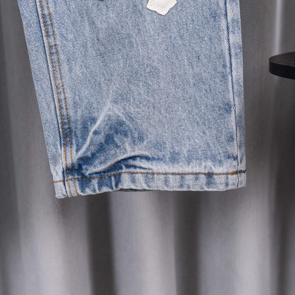 Light blue denim pants cuff with frayed hem and orange stitch detail