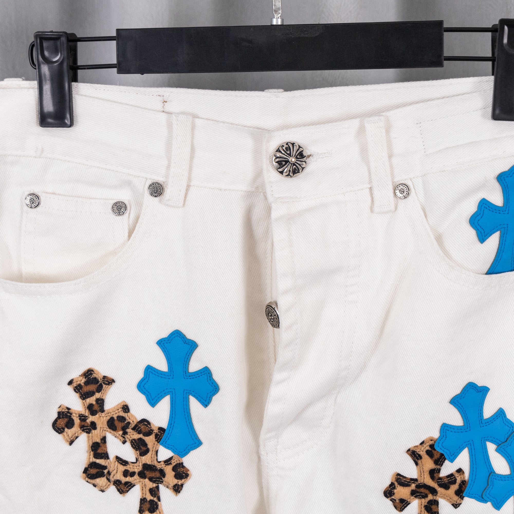 White pants with silver button and blue cross-and-leopard appliques, waistband close-up