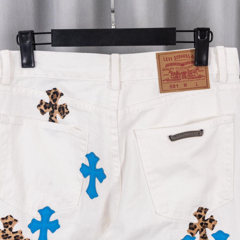 White jeans with blue cross and leopard patch graphics, front pocket close-up