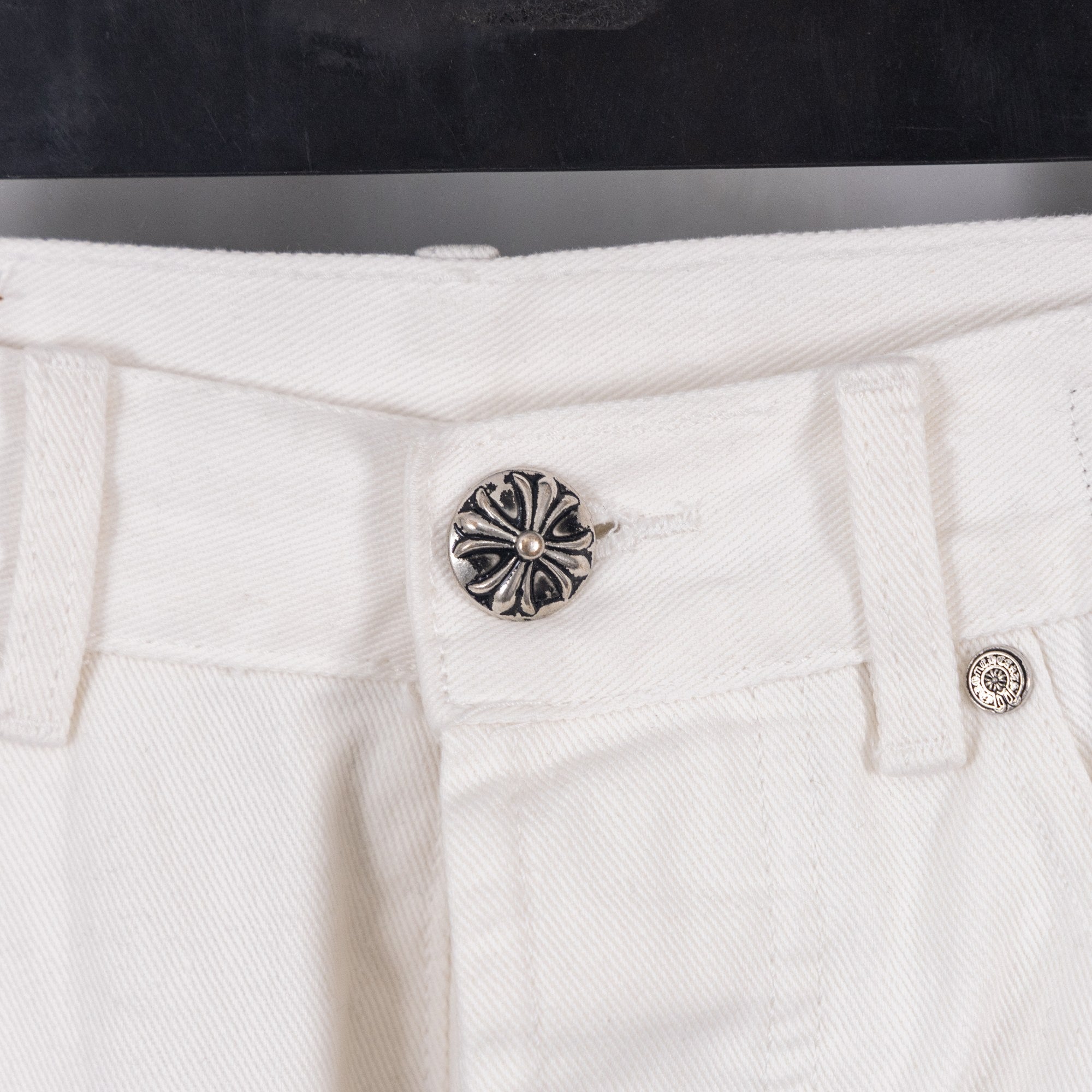 White pants with silver rivet button at waistband, centered close-up