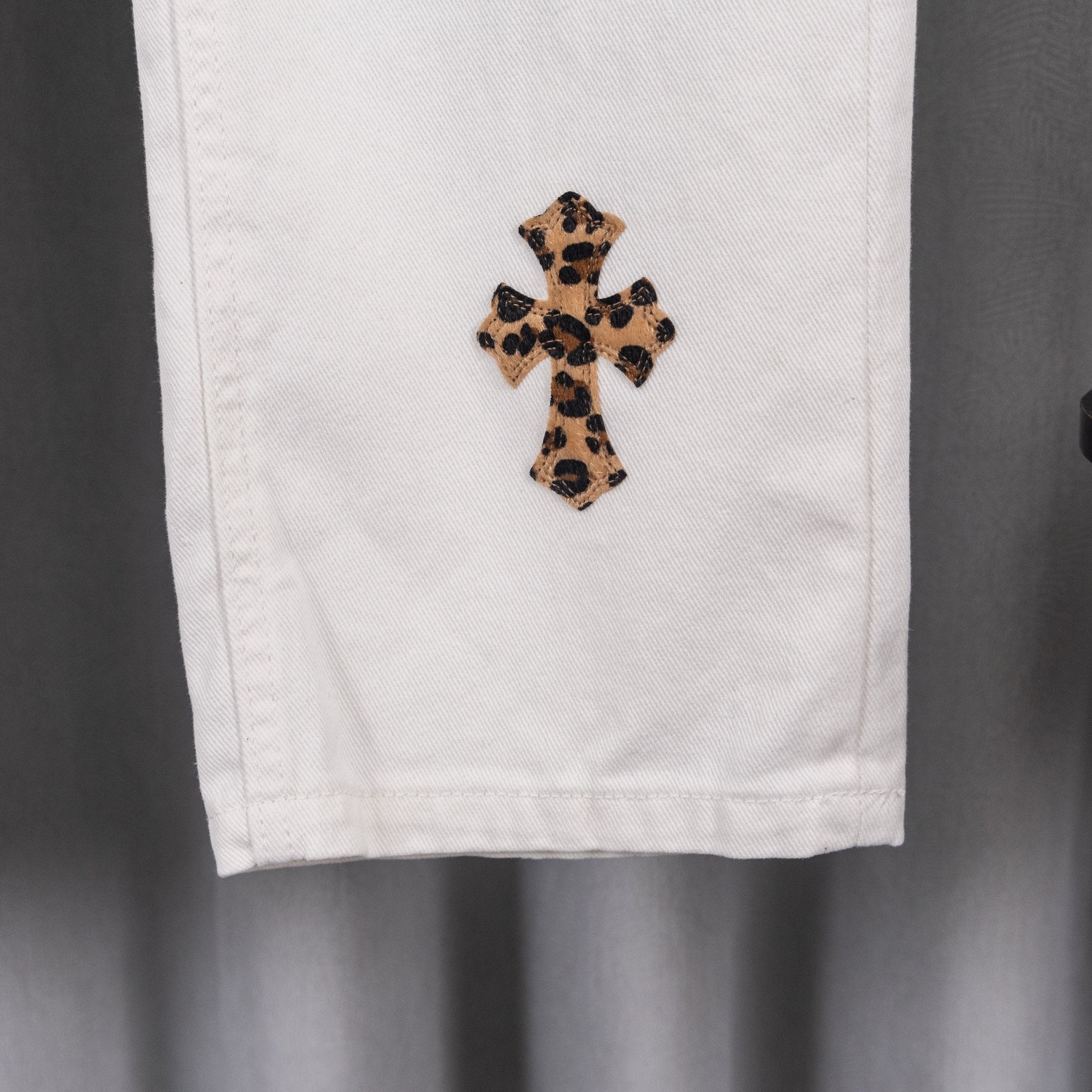 White pants cuff with leopard cross applique patch, lower-leg close-up