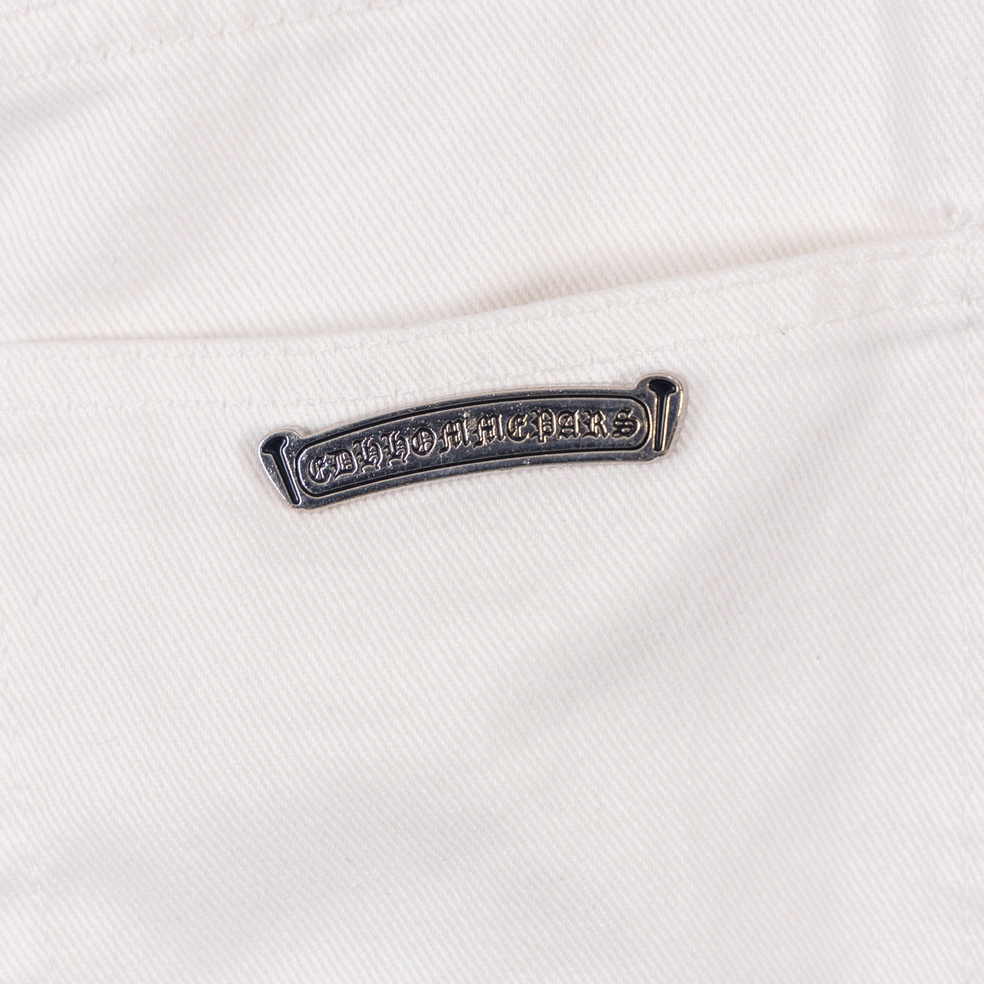 Pants metal logo bar on white denim near belt loop