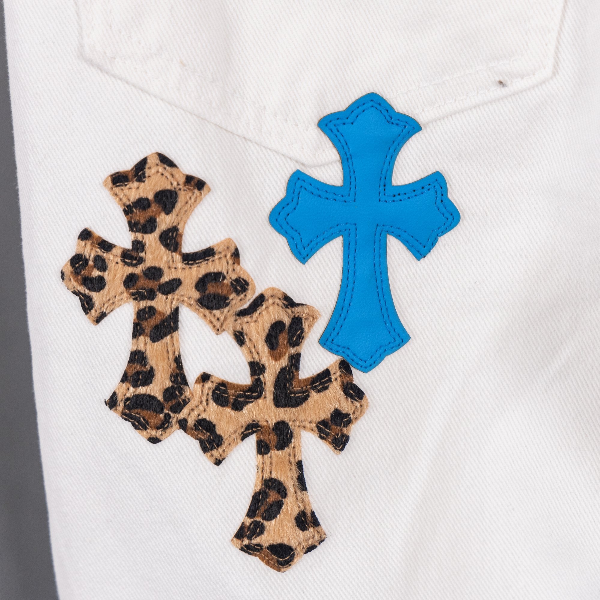 Chrome pants with leopard print cross patch and blue cross appliques on white denim