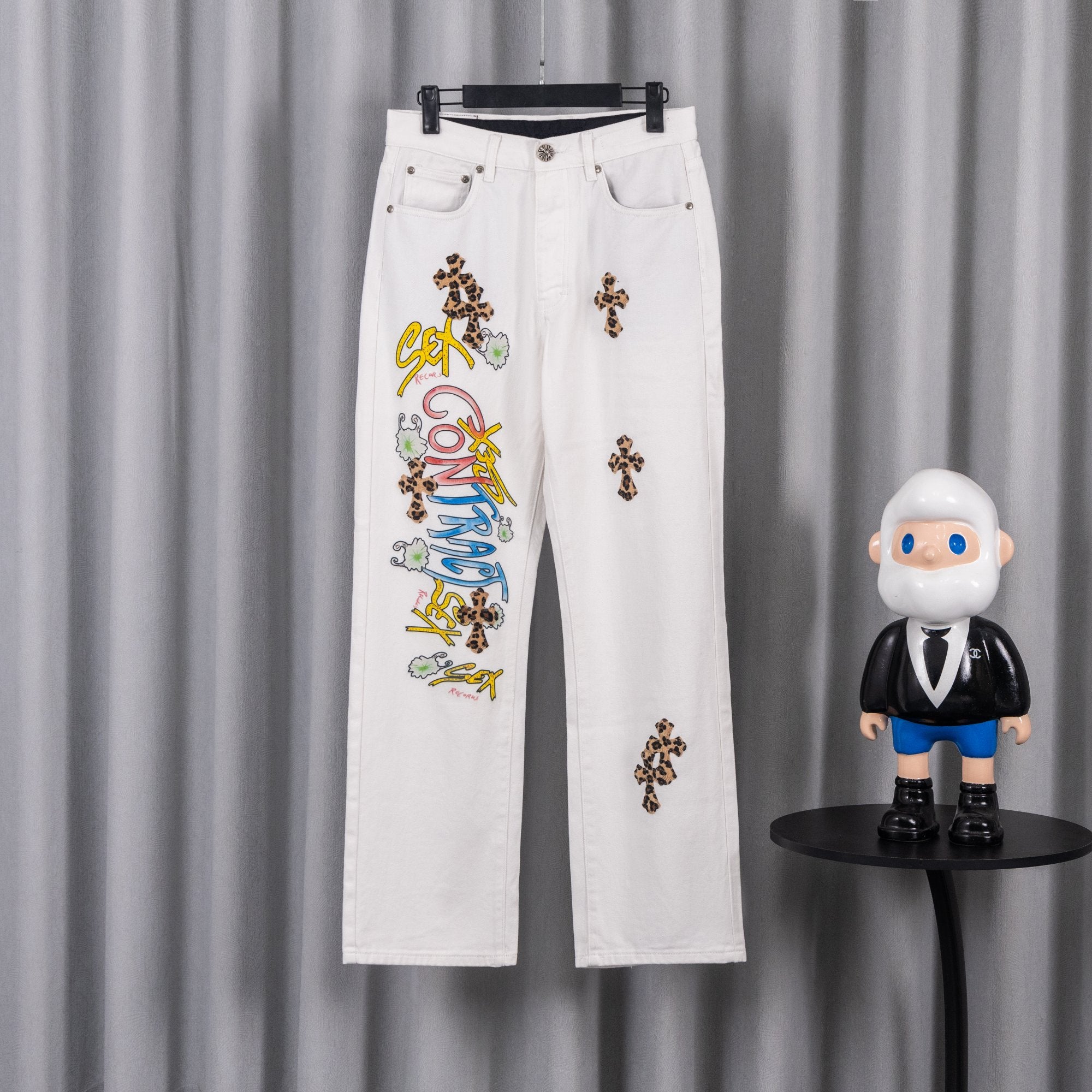 White denim pants with colorful graphic text and small cross patches