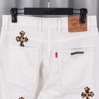 White denim pants front with cross patches, back pockets, and leather logo patch