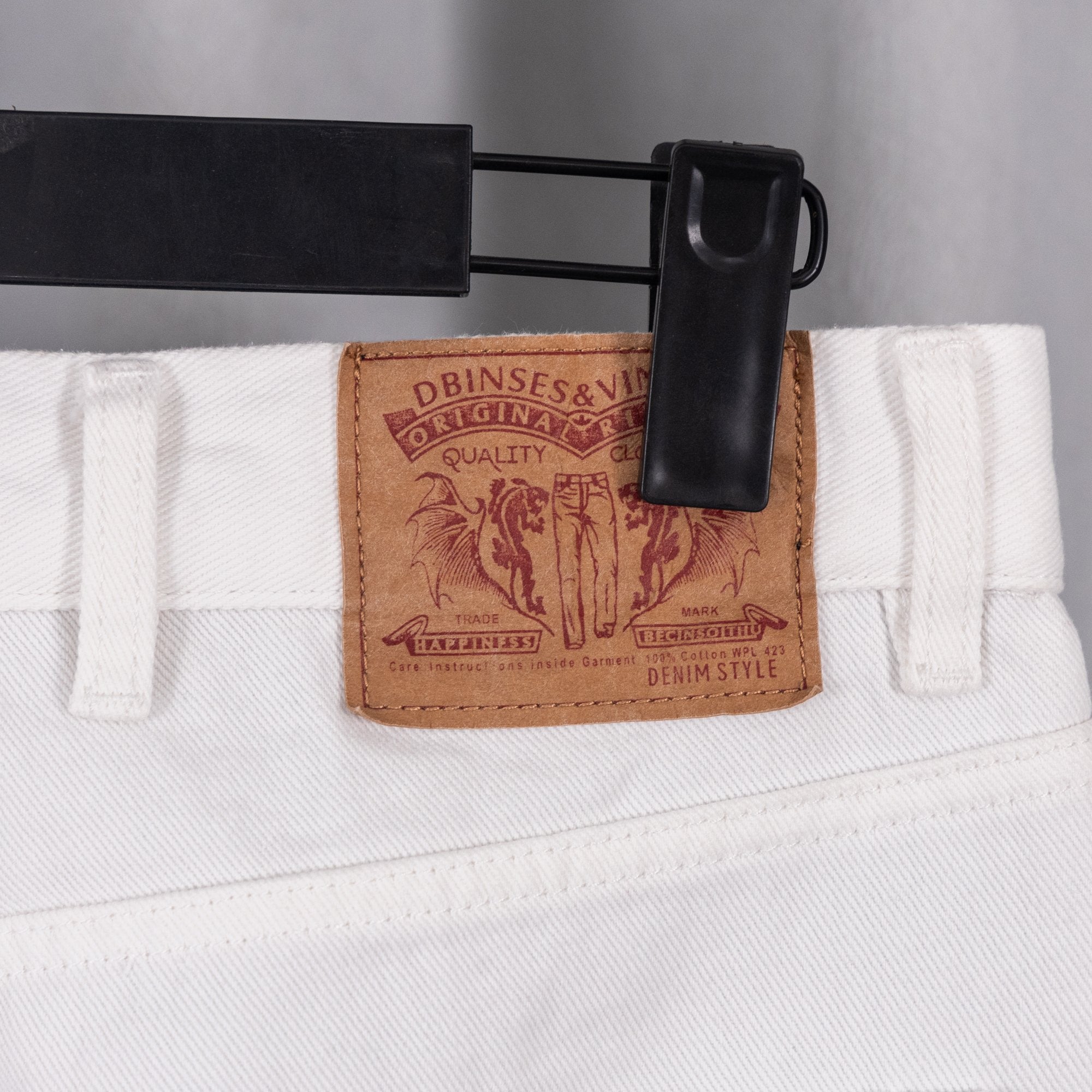 White denim pants waistband with leather logo patch and metal button hardware