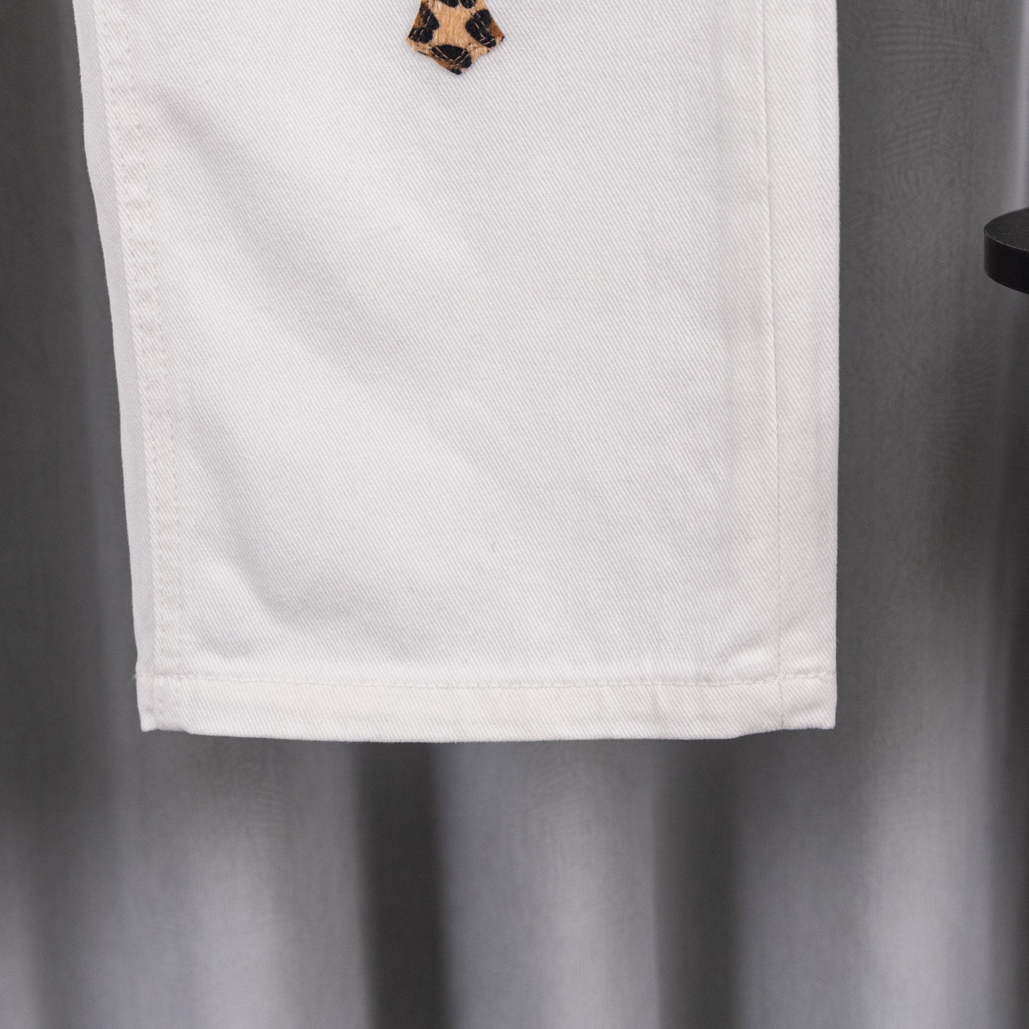 White denim pants with leopard cross patch near hem