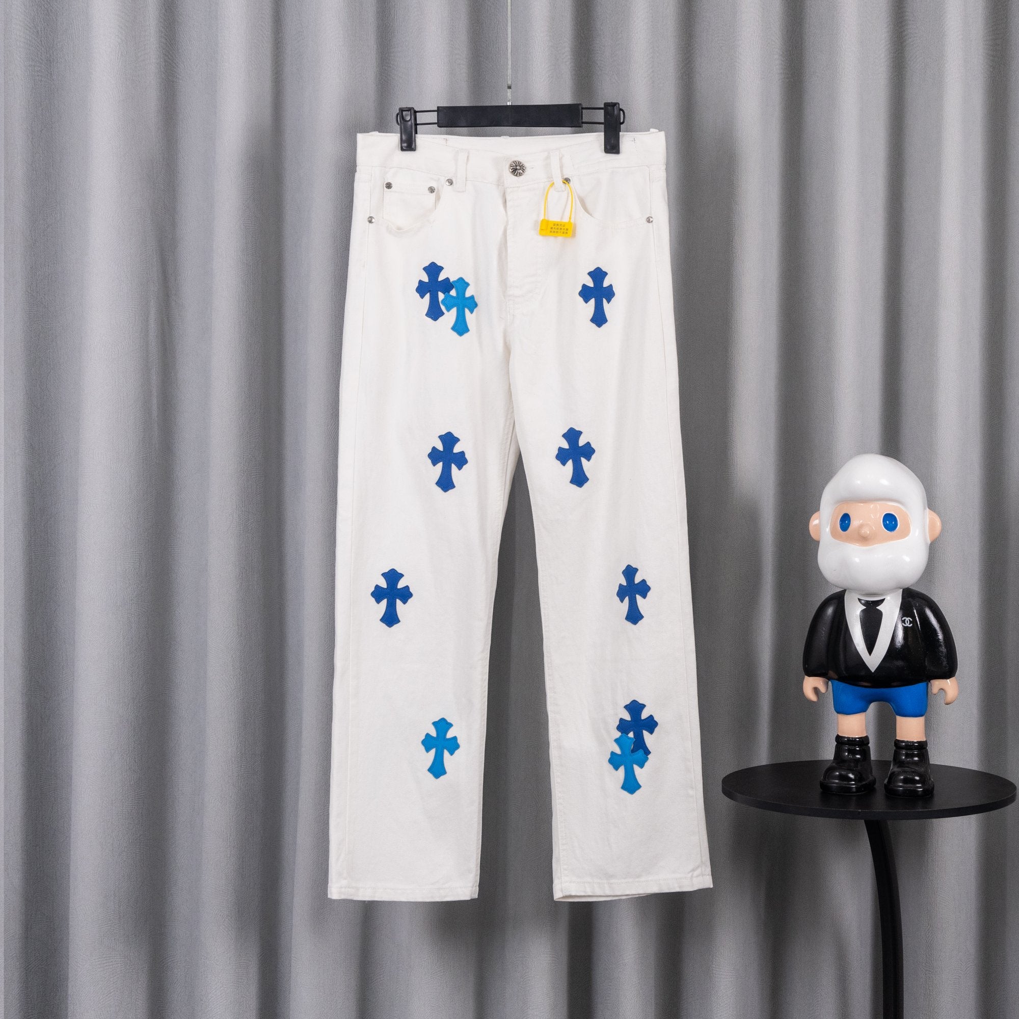 White denim pants with blue cross graphic print, front view on hanger