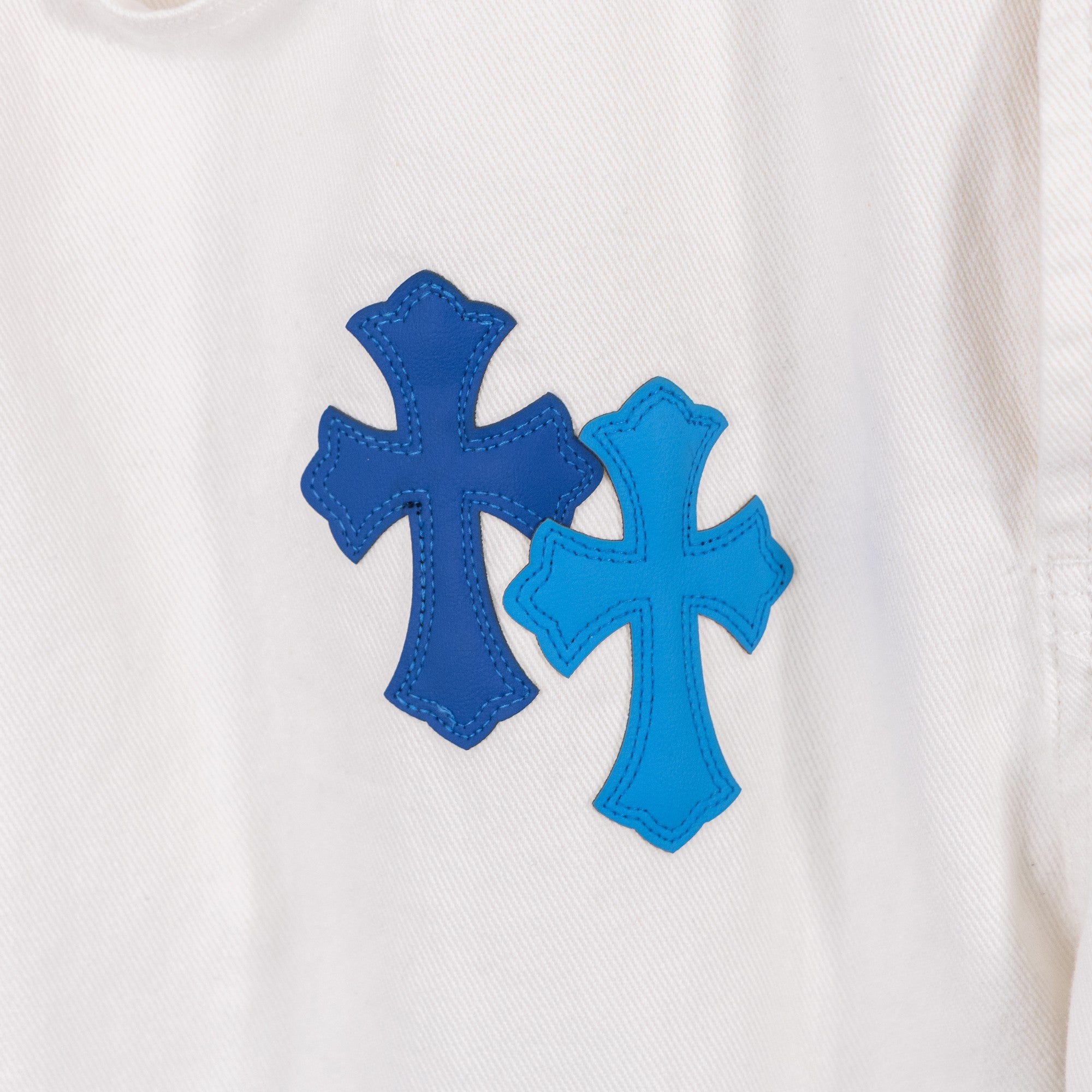 White denim pants with embroidered blue cross patches, close-up