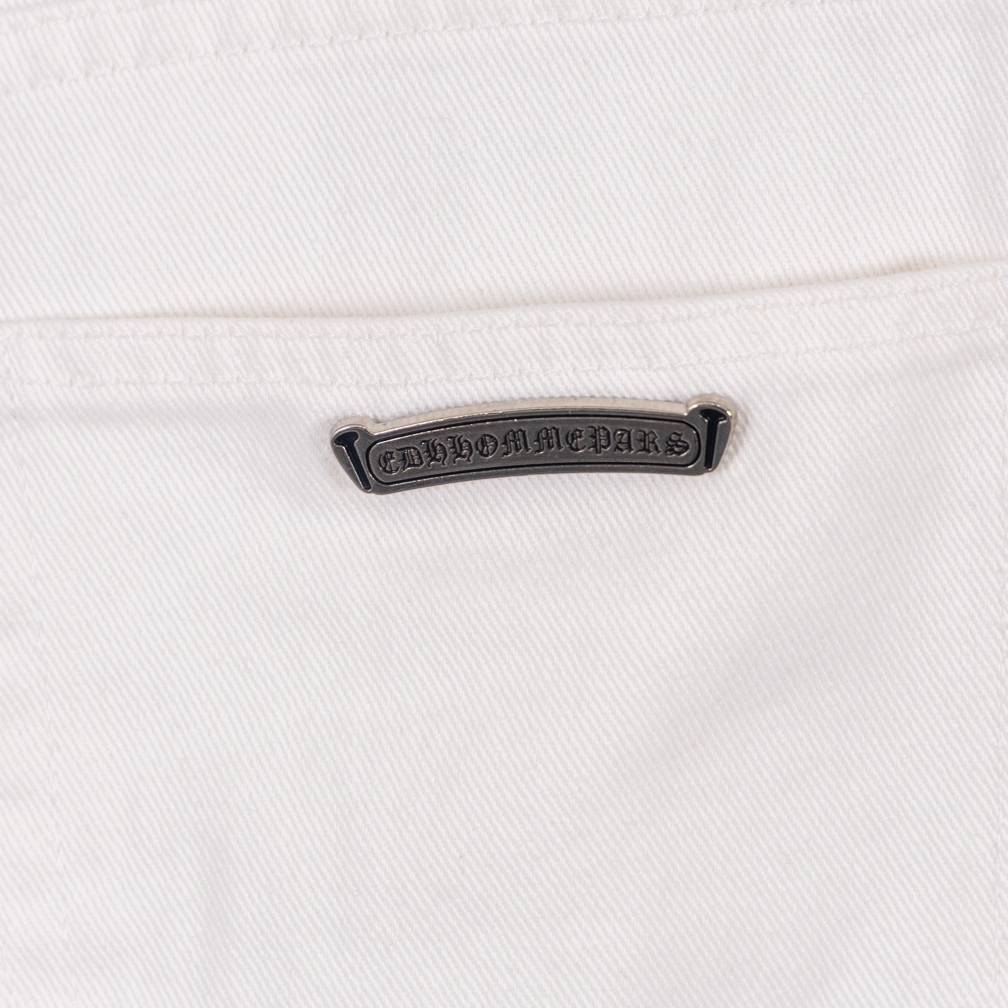 White denim pants with embossed logo label patch at waistband, close-up