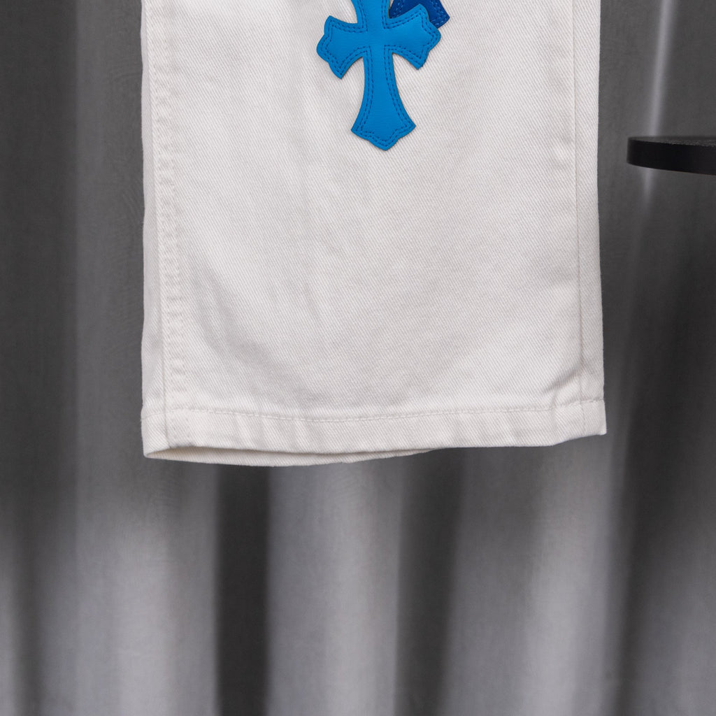White denim pant leg hem with blue cross patch, partial view