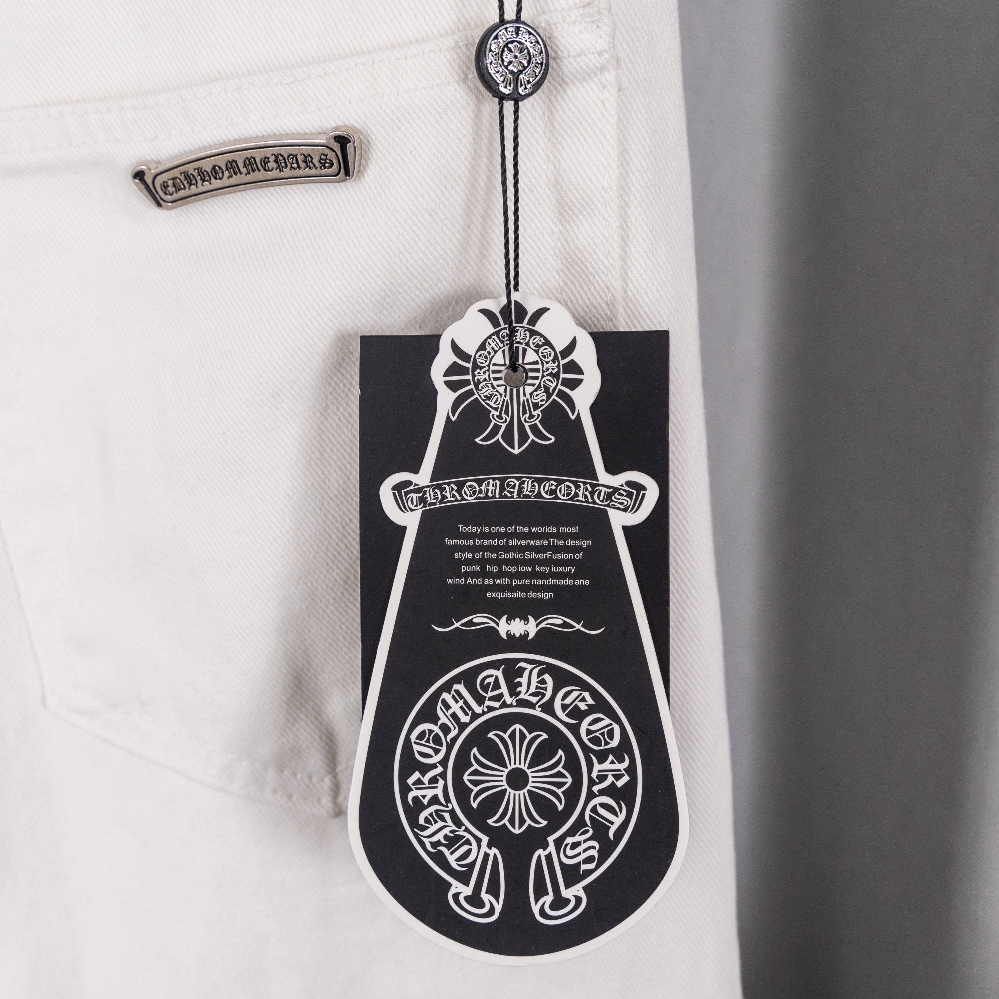 White denim pants with hang tag and decorative patch at waist, close-up
