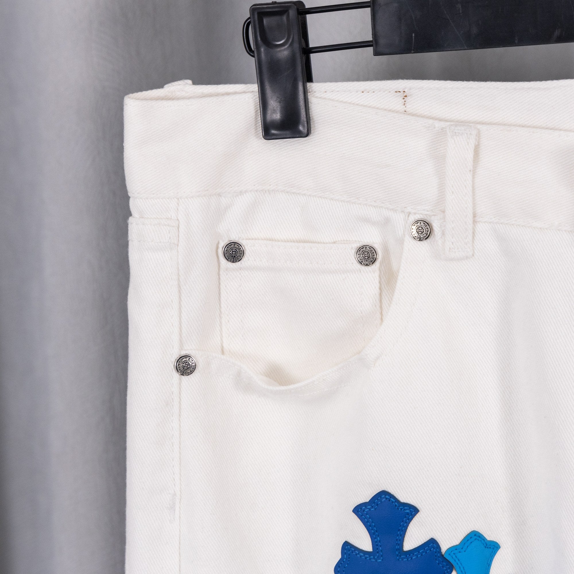White denim pants with front coin pocket and blue cross patch on leg