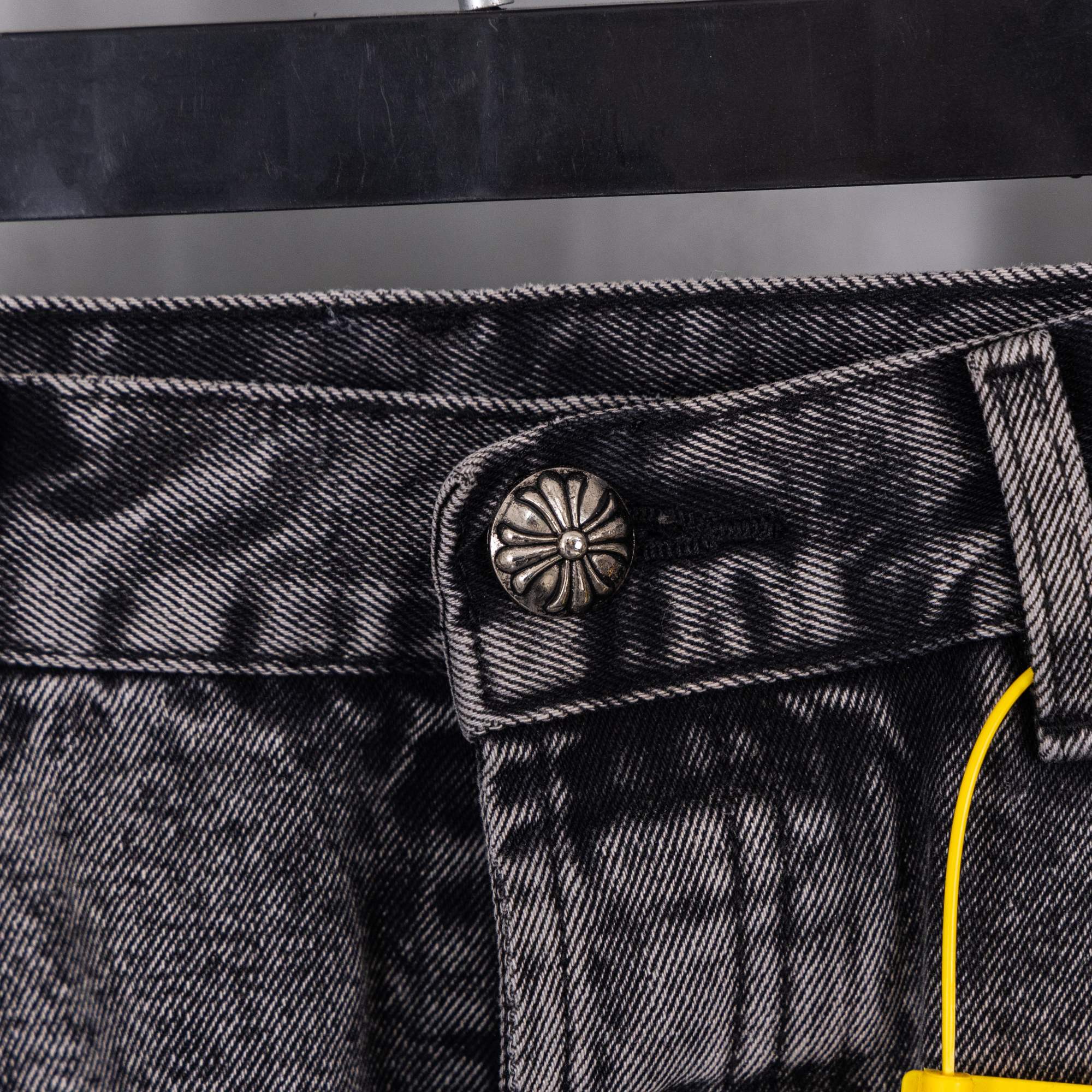Dark gray denim waistband button and front pocket seam detail with yellow pull