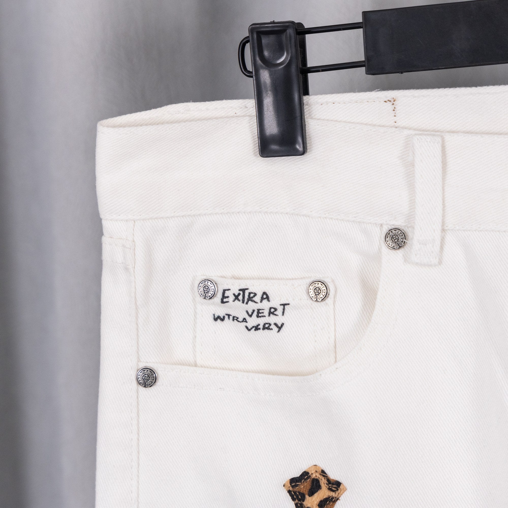 White pants with “Extra Vert Very” label and leopard-print cross applique