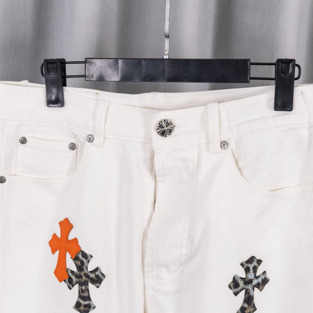 White denim pants waistband with button and orange/black cross design on leg