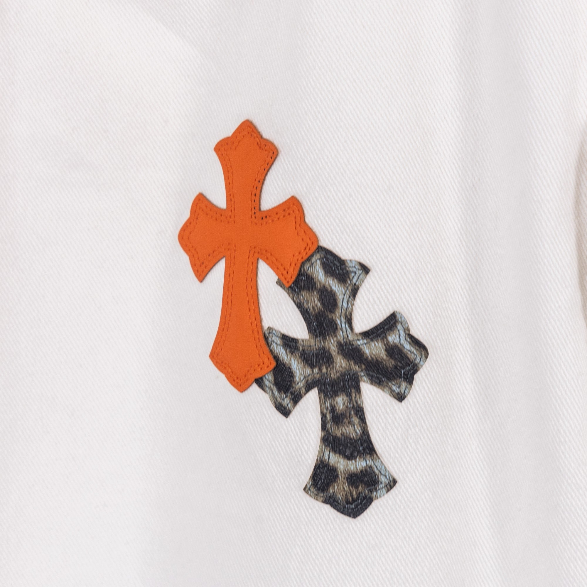 Orange cross applique with black pattern backing on white denim pants