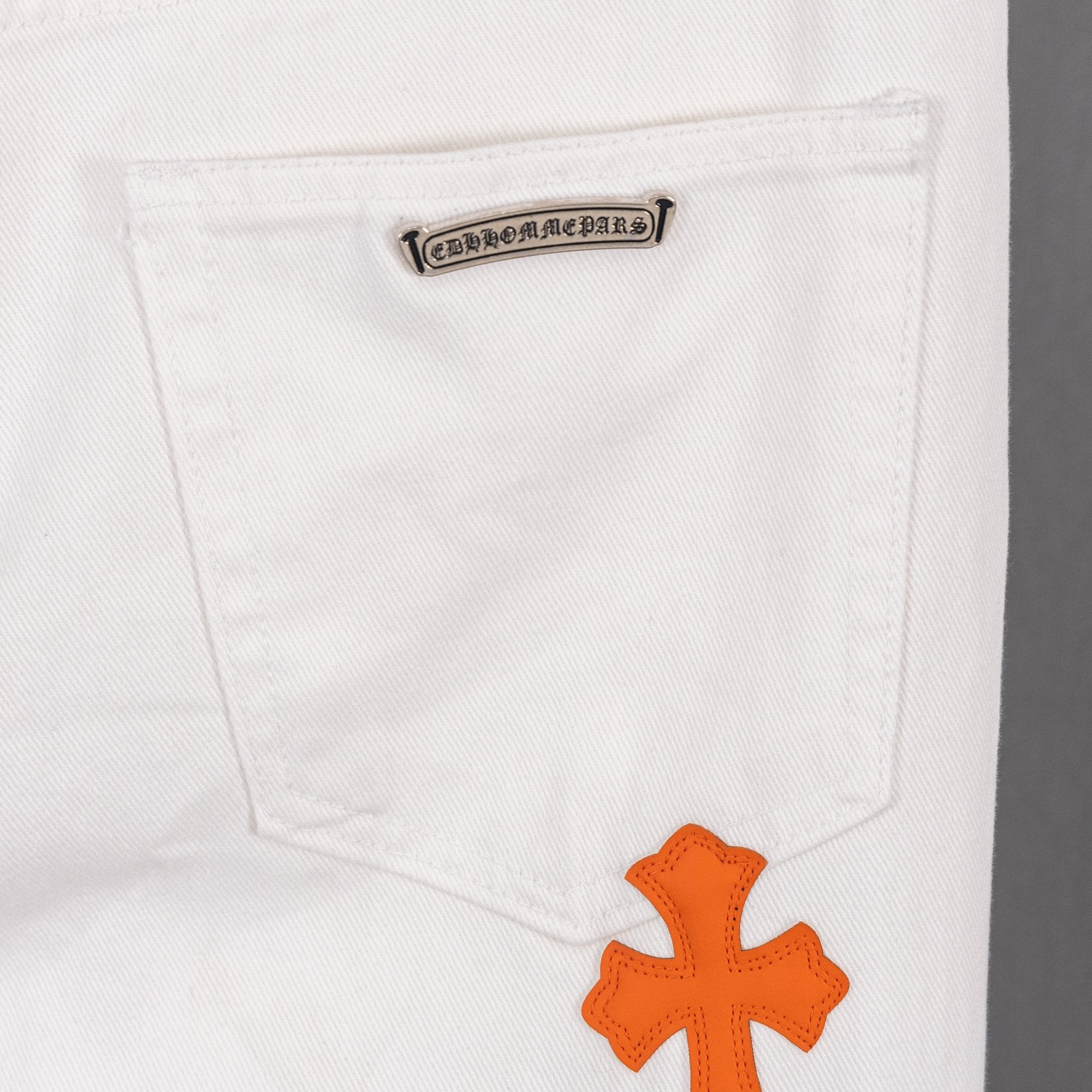 White denim pants pocket with small logo patch and orange cross applique