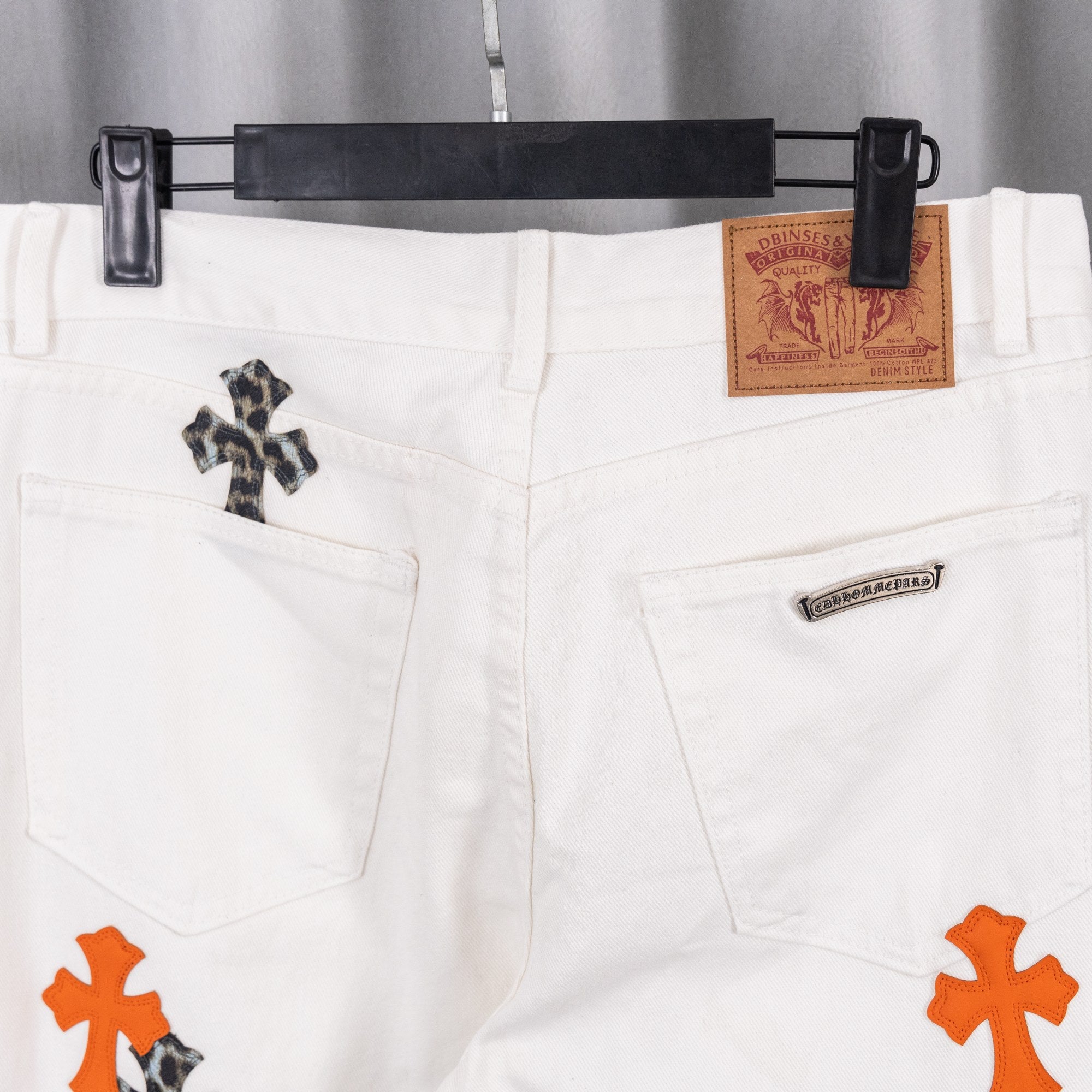 White chrome pants front view with side pockets and orange cross appliqué