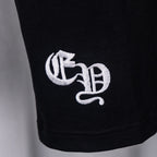 Black T-shirt close-up of embroidered white letter emblem near the hem