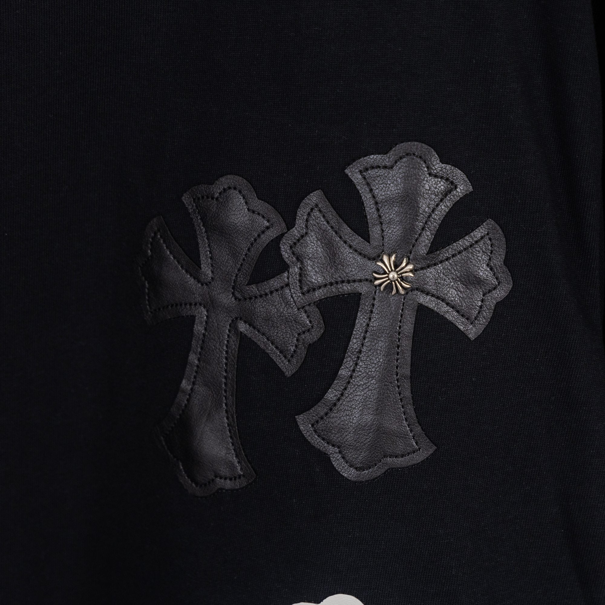 Black T-shirt with dark gray embroidered cross applique cluster.