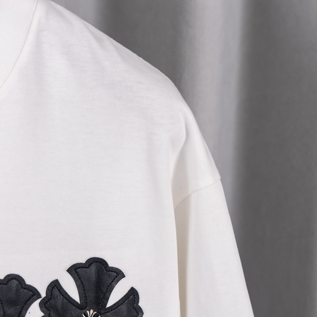 White T-shirt side with small black cross applique on sleeve