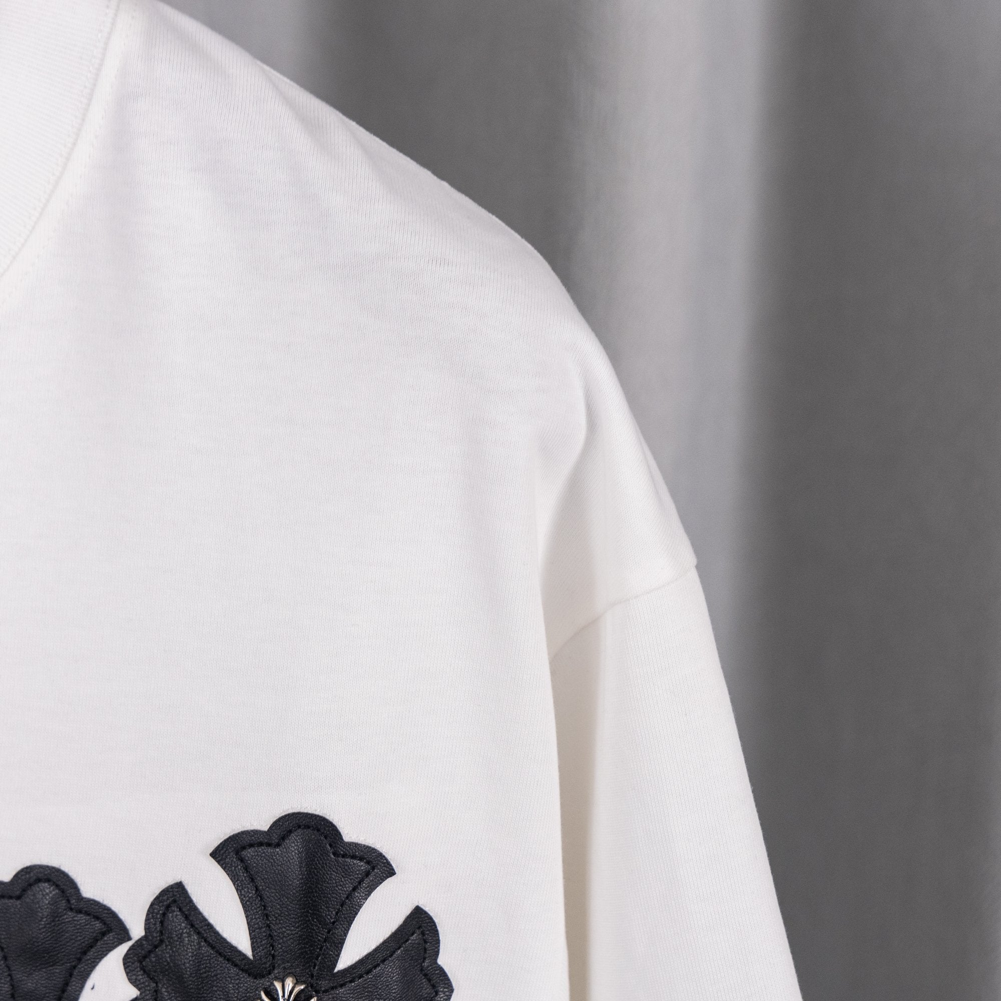 White T-shirt side with small black cross applique on sleeve