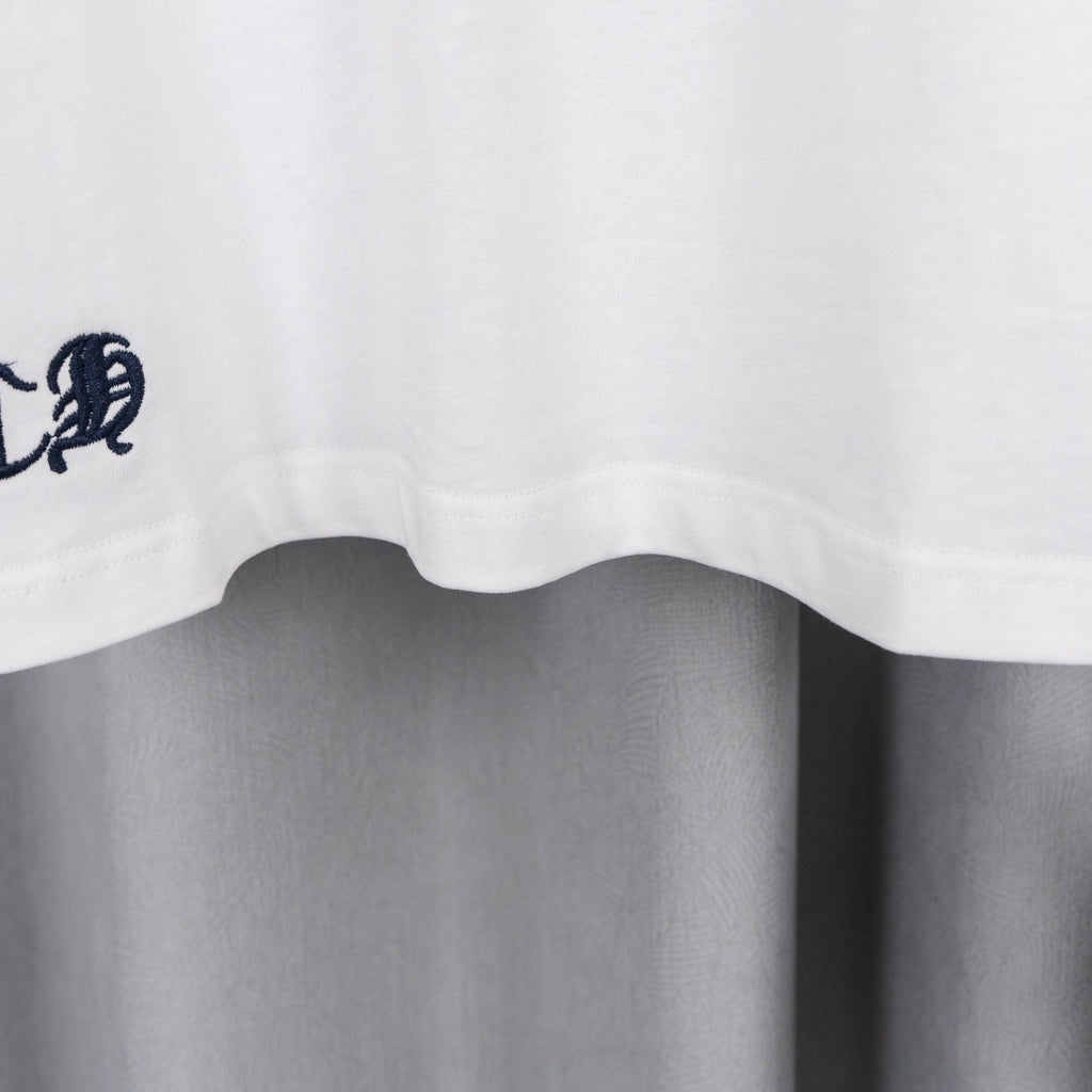 White T-shirt hem with small embroidered crest near the bottom edge