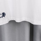White T-shirt hem with small embroidered crest near the bottom edge