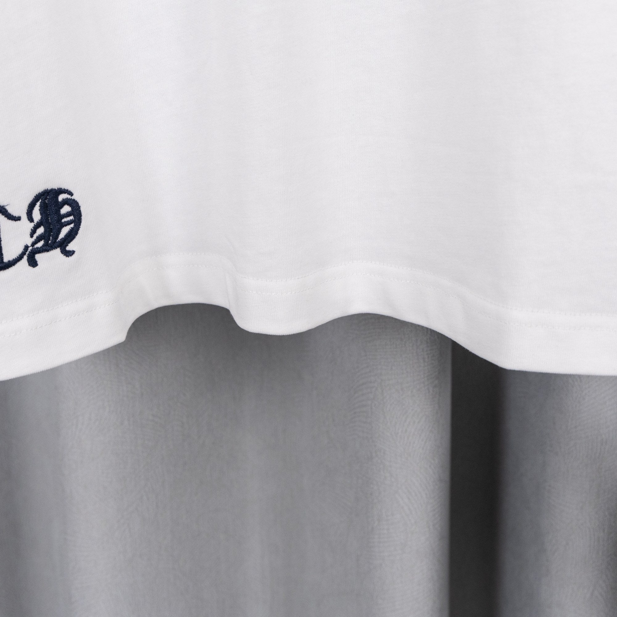 White T-shirt hem with small embroidered crest near the bottom edge