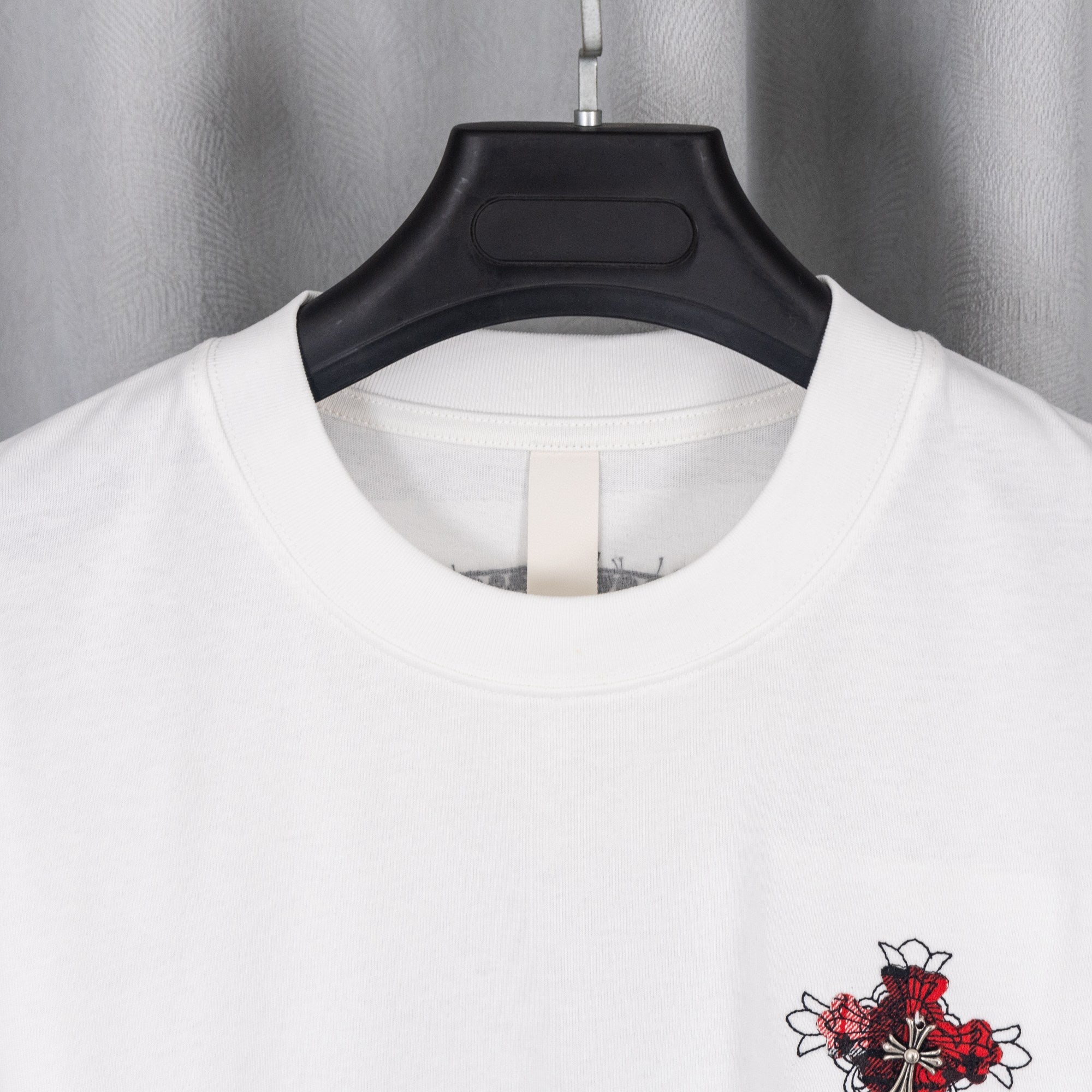 White crew-neck T-shirt neckline on hanger with small red cross graphic