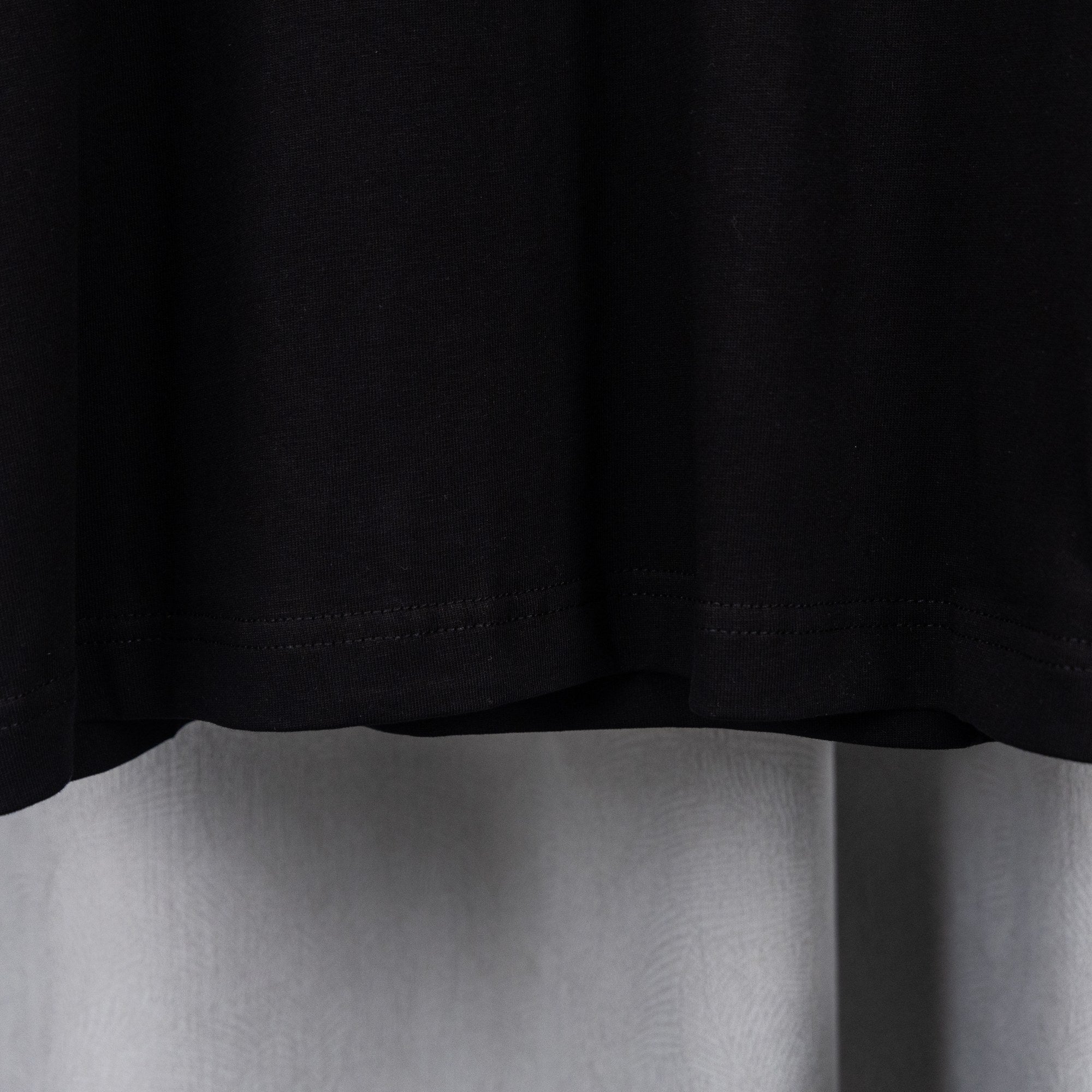 Black T-shirt bottom hem with visible stitching.