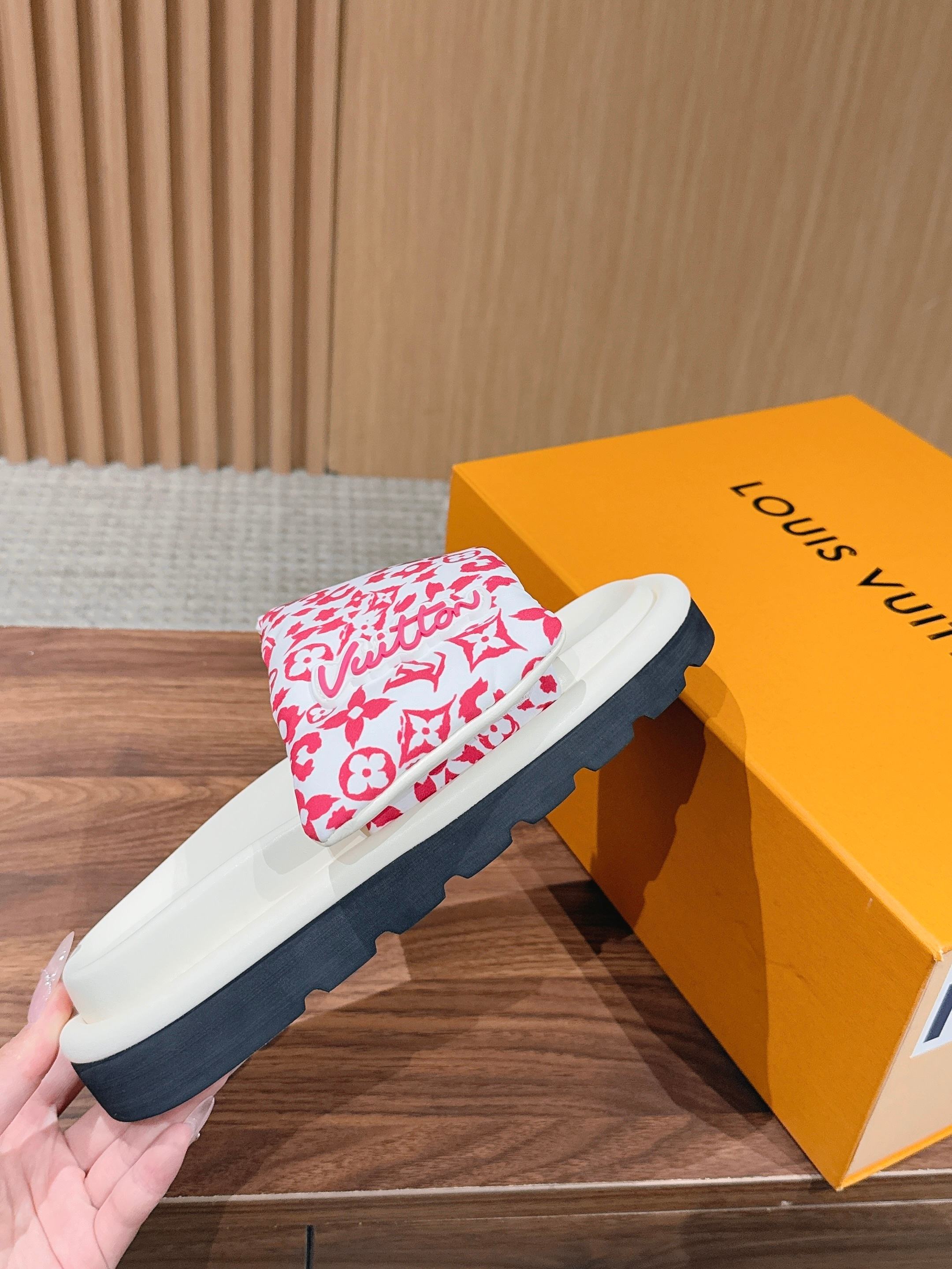 Pink floral logo-pattern slide sandal held near a yellow Louis Vuitton shoebox