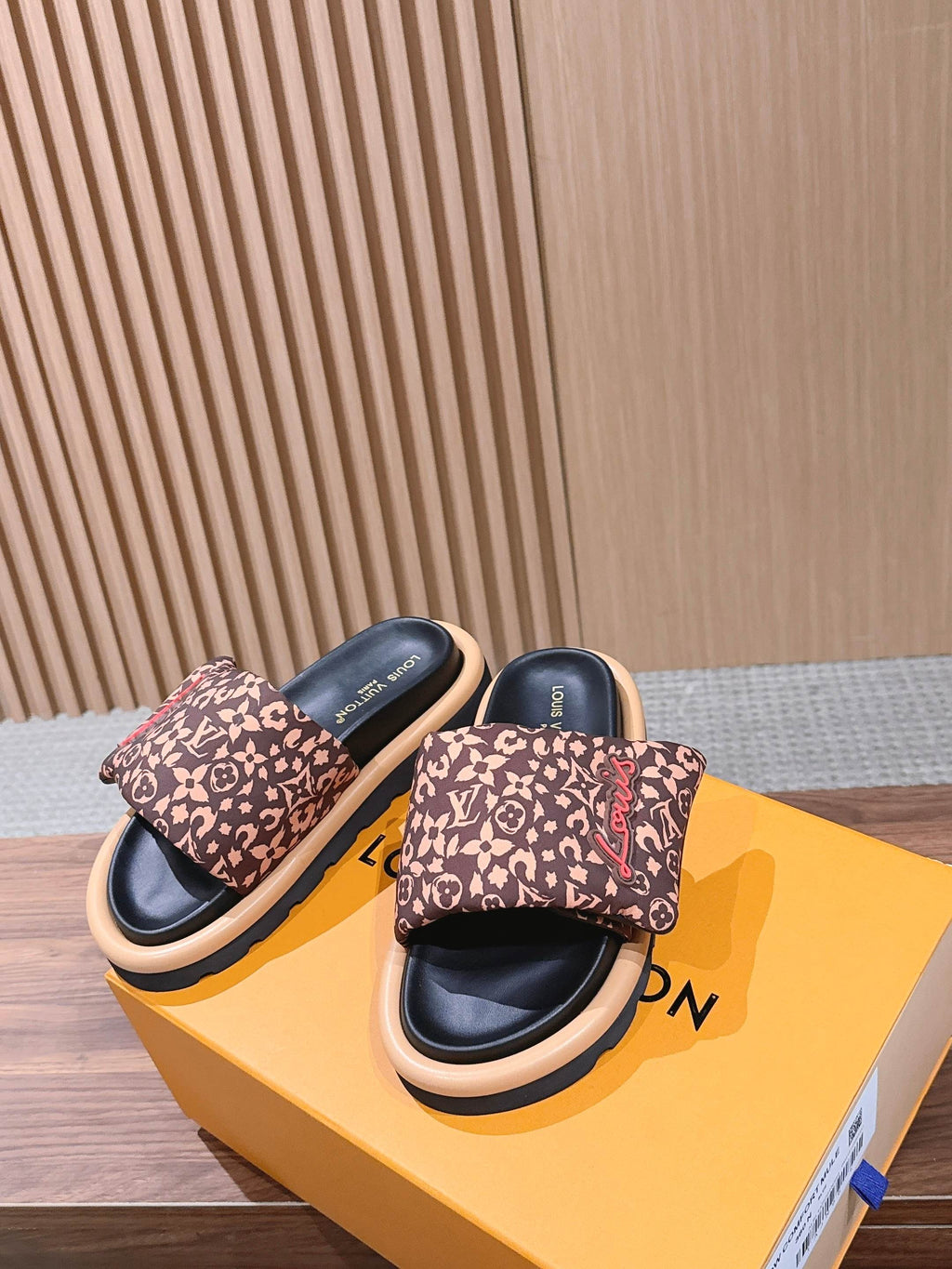 Louis Vuitton monogram slide sandals with beige edging, resting on orange box