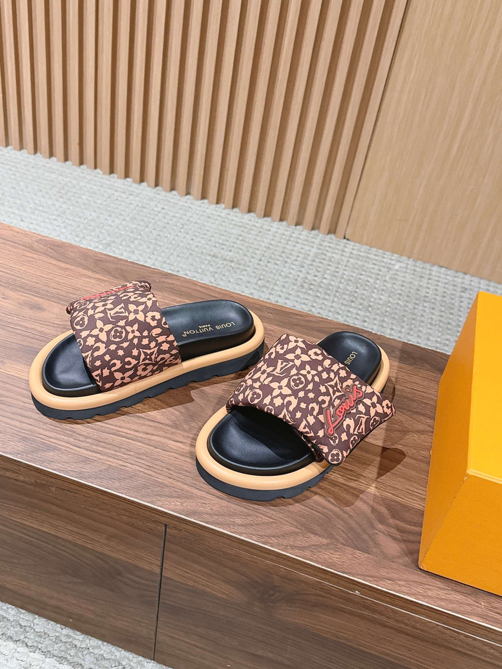 Printed slide sandals, dark logo-patterned straps with light edges and black soles.