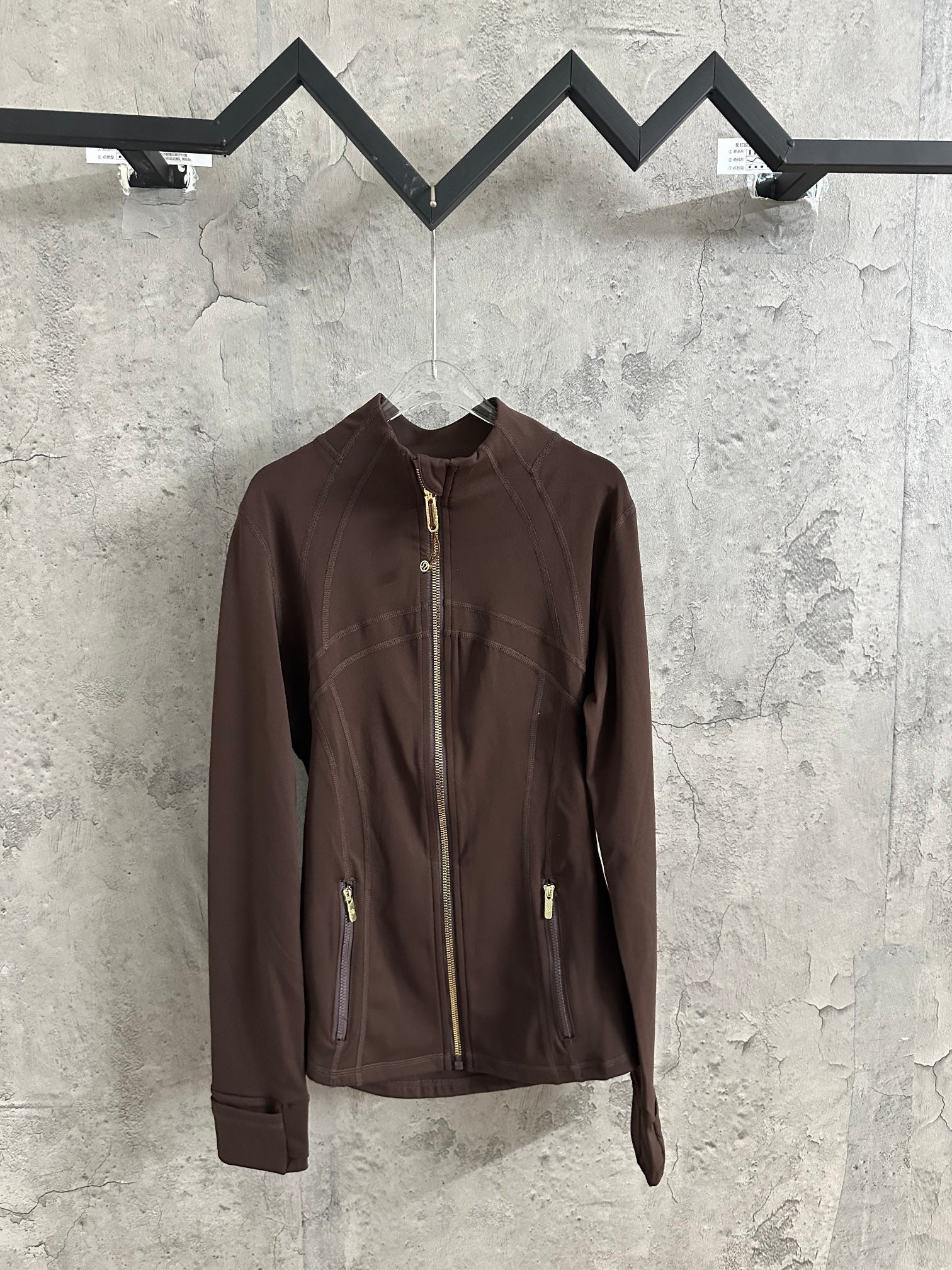 Brown zip-up jacket with stand collar and gold-tone front zipper, hanging on a rack