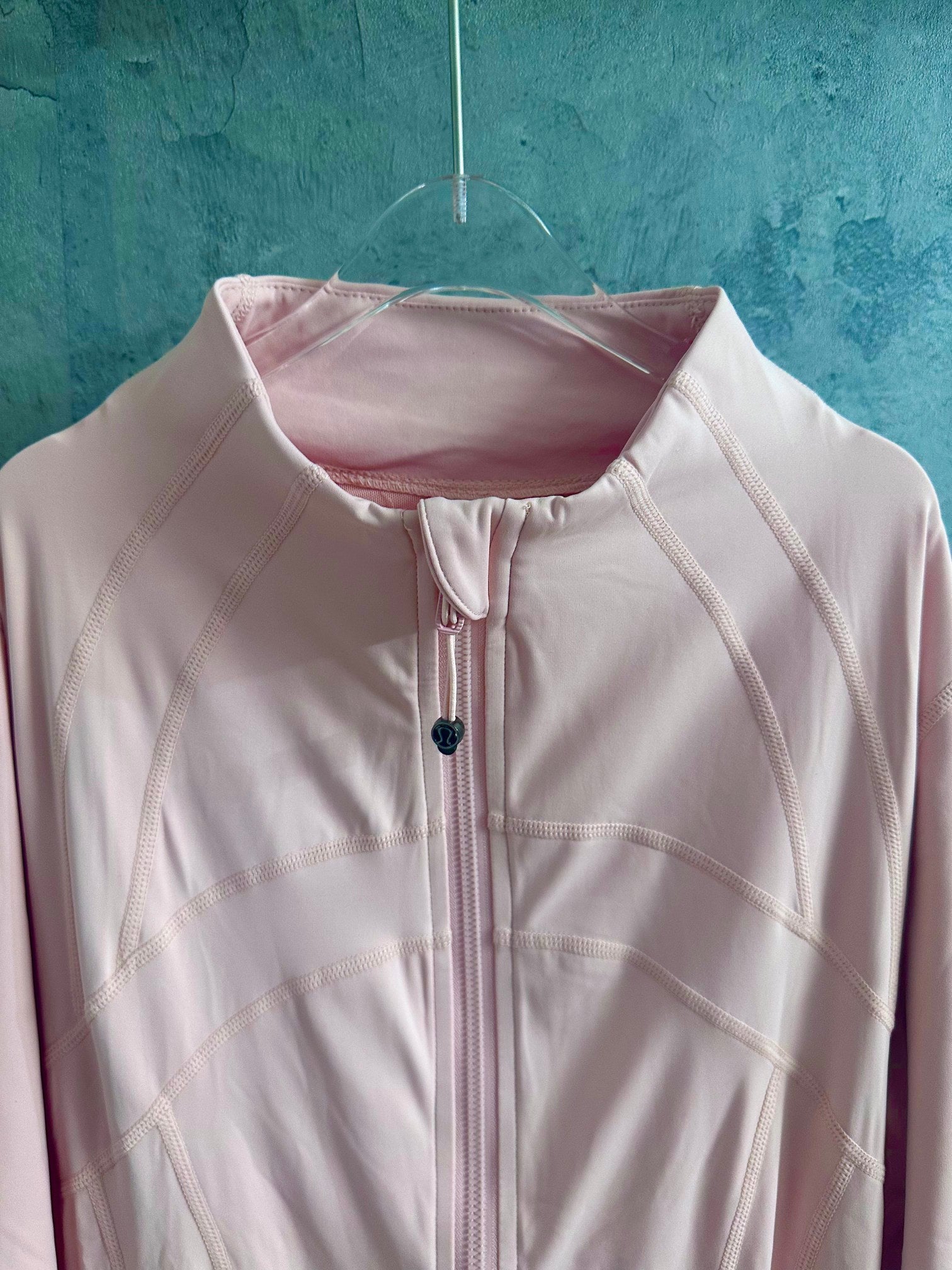 Light pink zip-up jacket with stand collar, zipper, and small chest emblem
