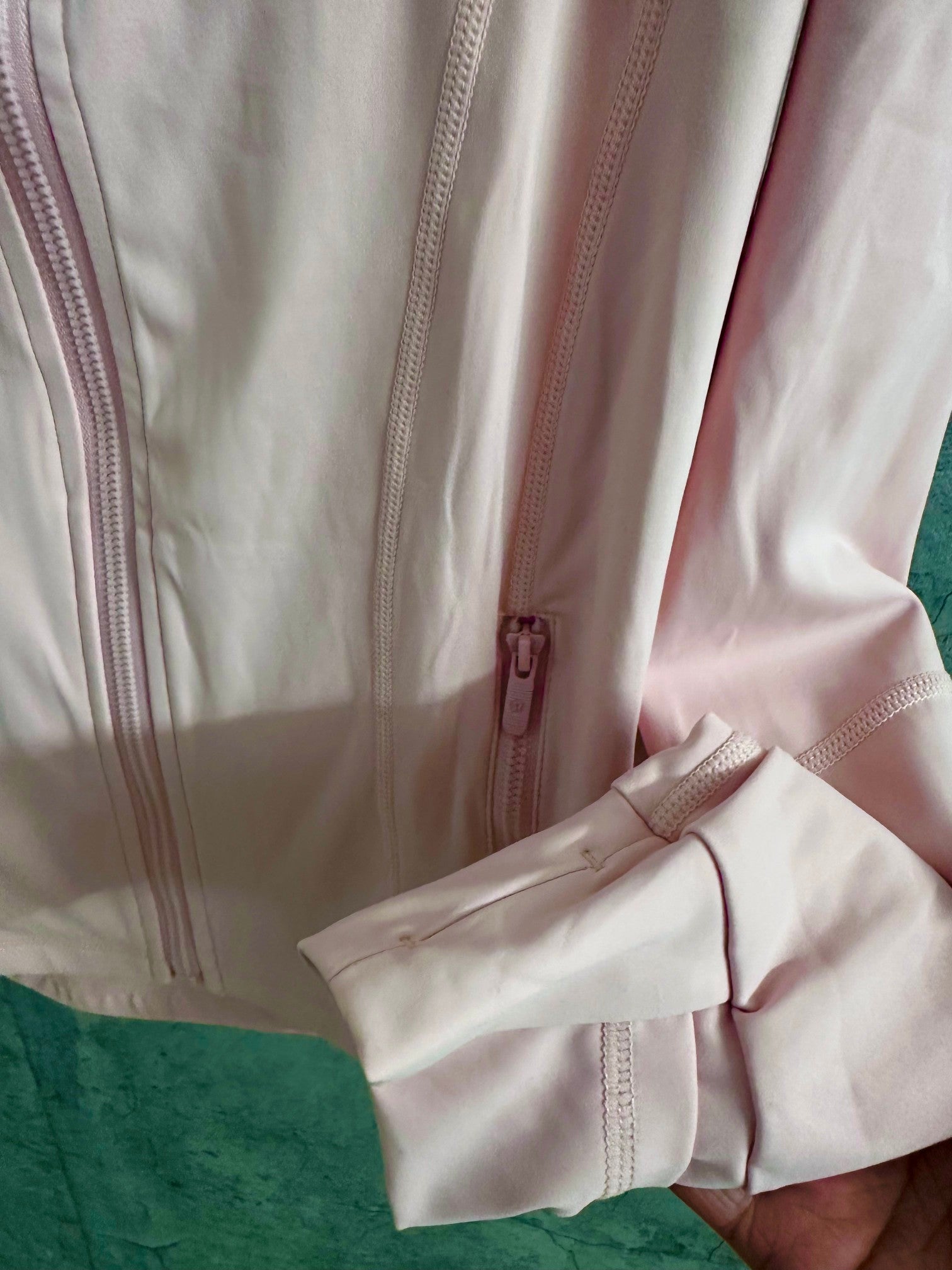 Light pink zip-up jacket cuff with zipper pull and stitched detail